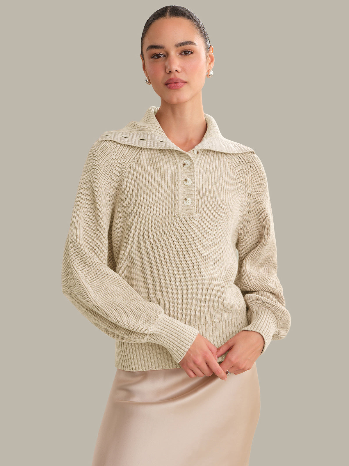 Woman wearing a beige ribbed sweater with a collar against a neutral background