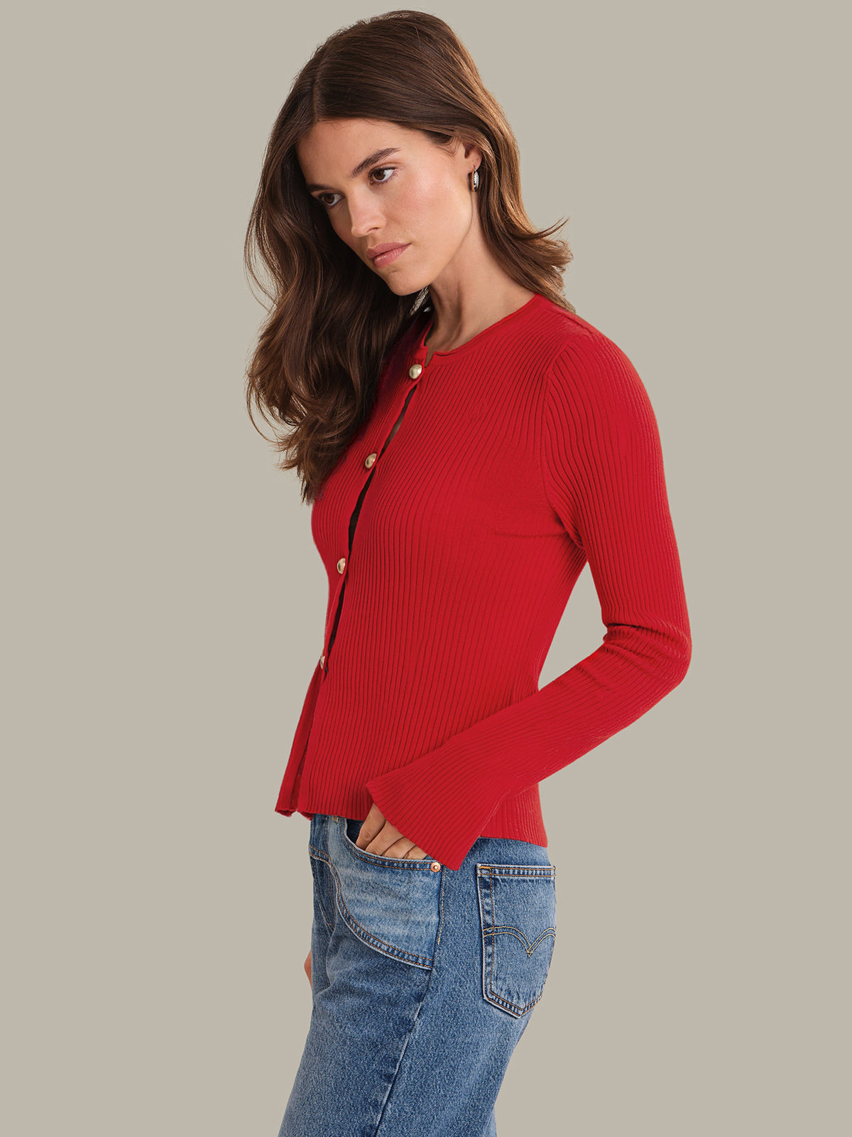 Woman wearing a red cardigan and blue jeans on a plain background