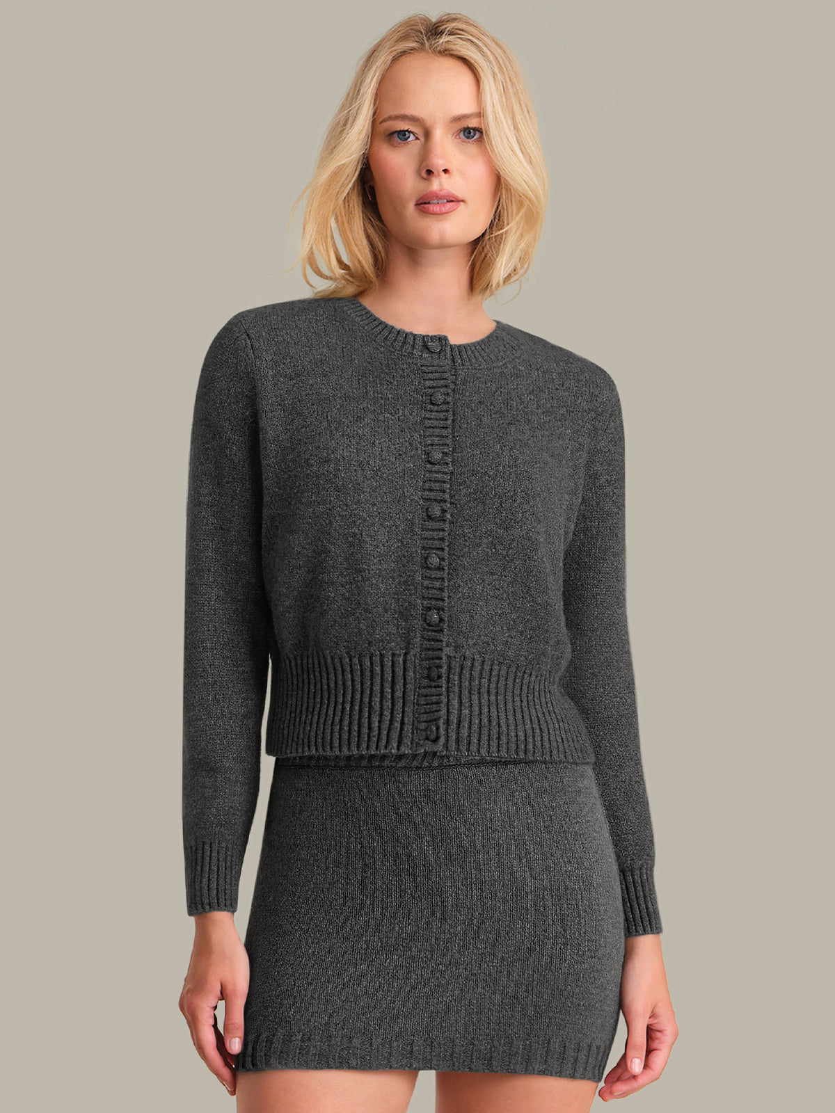 Woman wearing a gray knitted cardigan and skirt set against a plain background