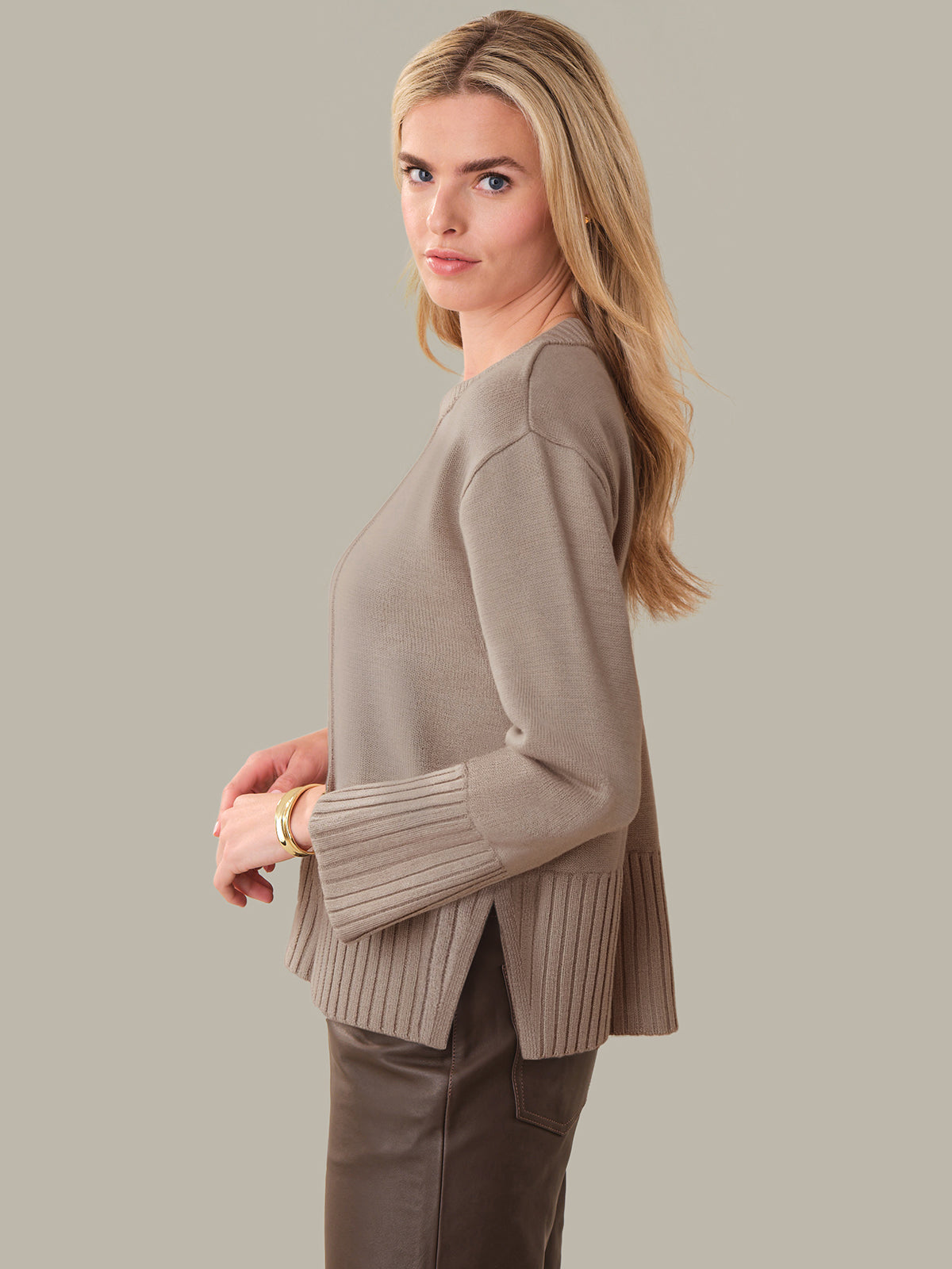 Woman wearing a beige sweater and pants against a plain background