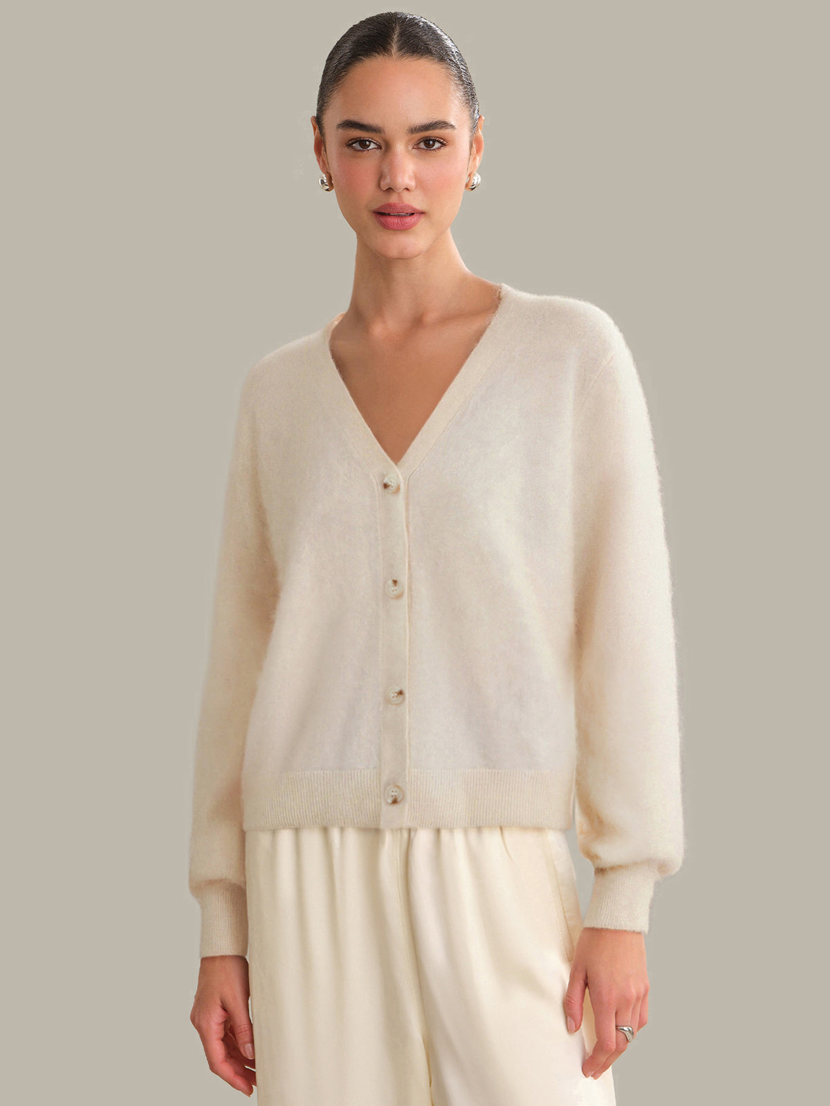 Woman wearing a cream cardigan over a white top with beige pants against a neutral background