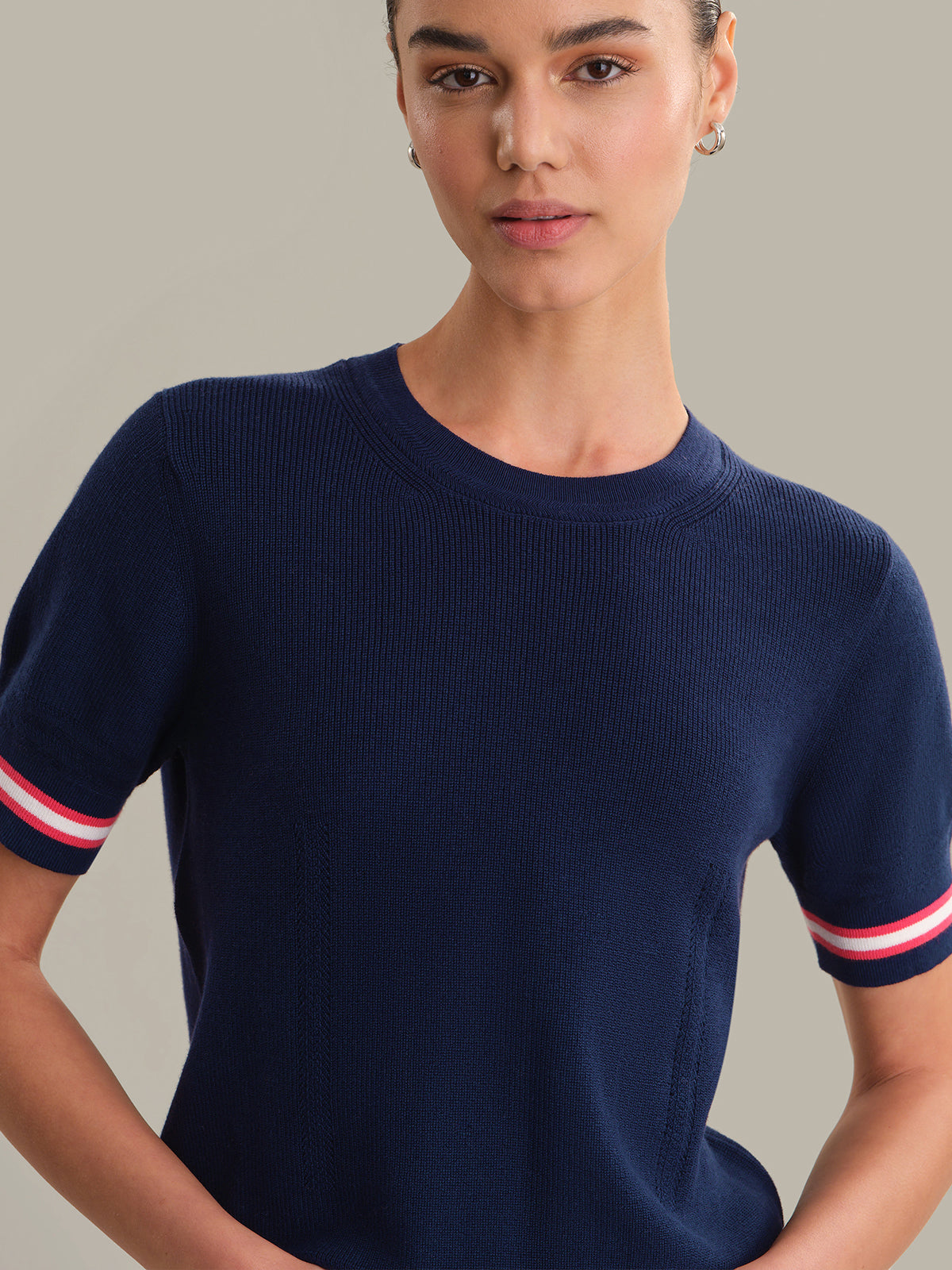 Woman wearing a navy blue sweater with red and white stripes on a neutral background