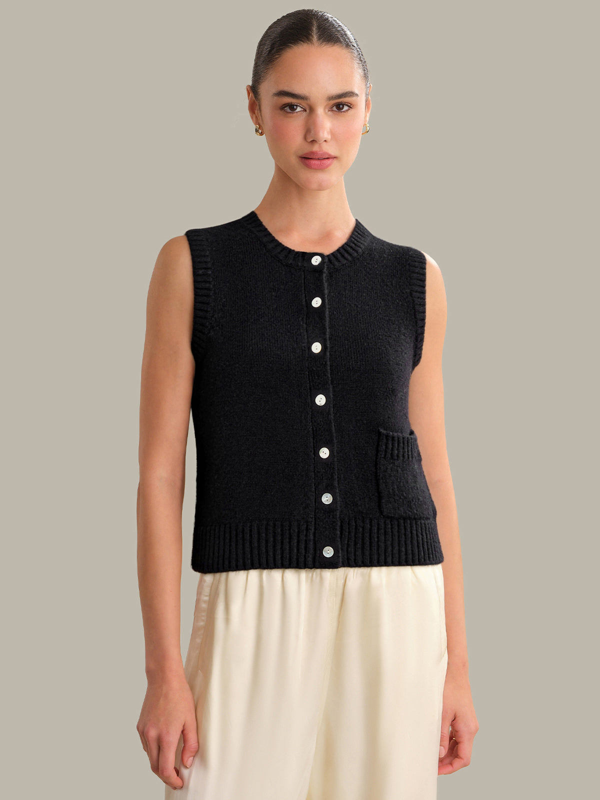 Woman wearing a black sleeveless knitted cardigan against a gray background