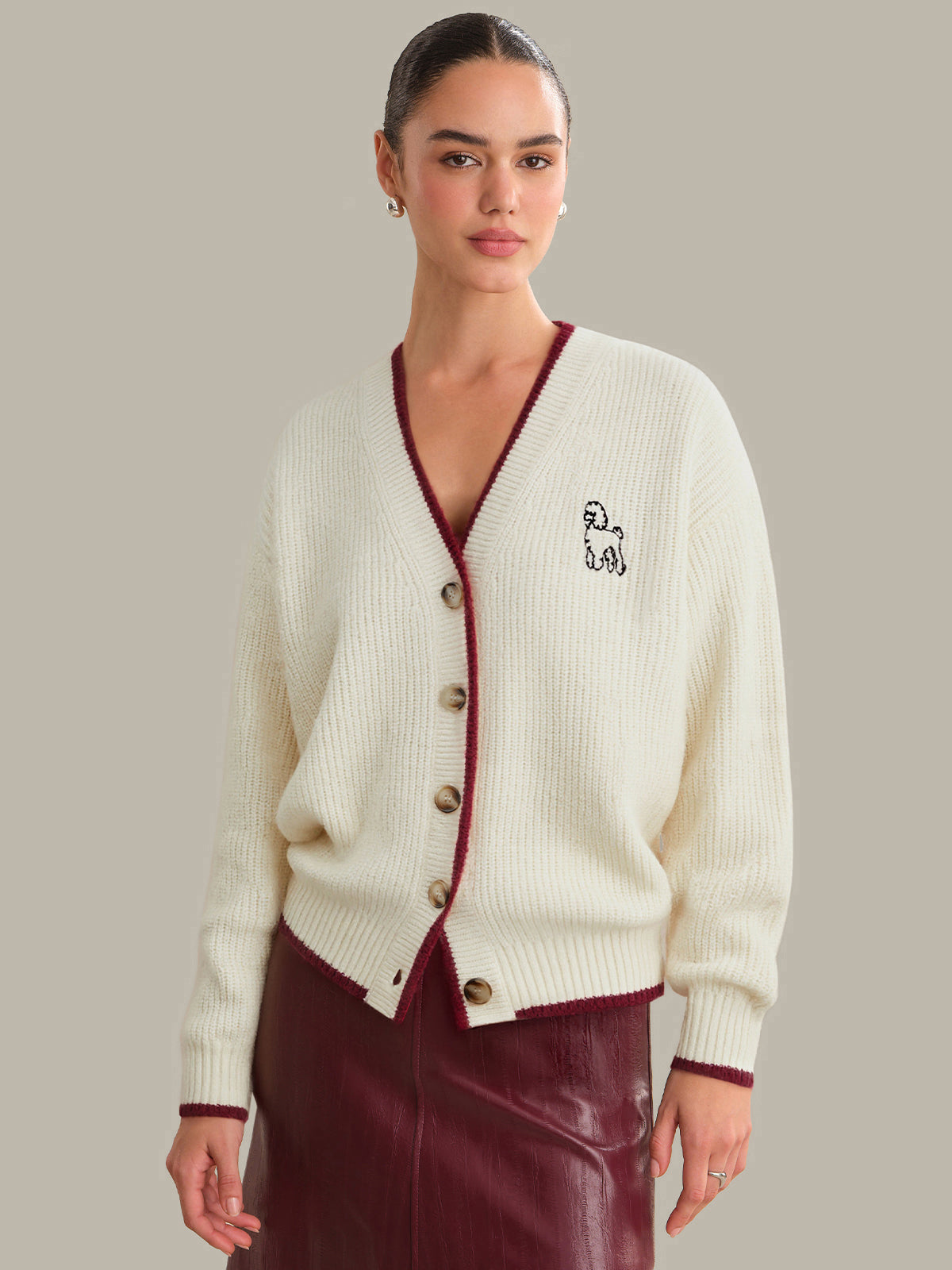 Woman wearing a cream cardigan with red trim and a logo on a plain background