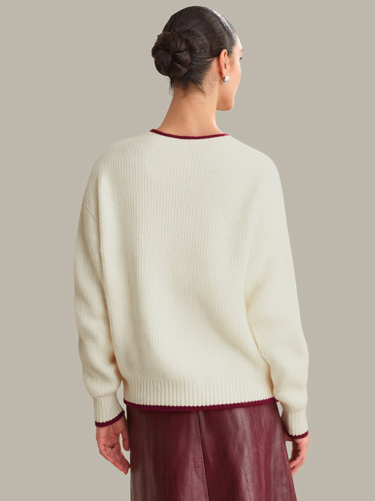 Person wearing a cream sweater with red trim on a plain background
