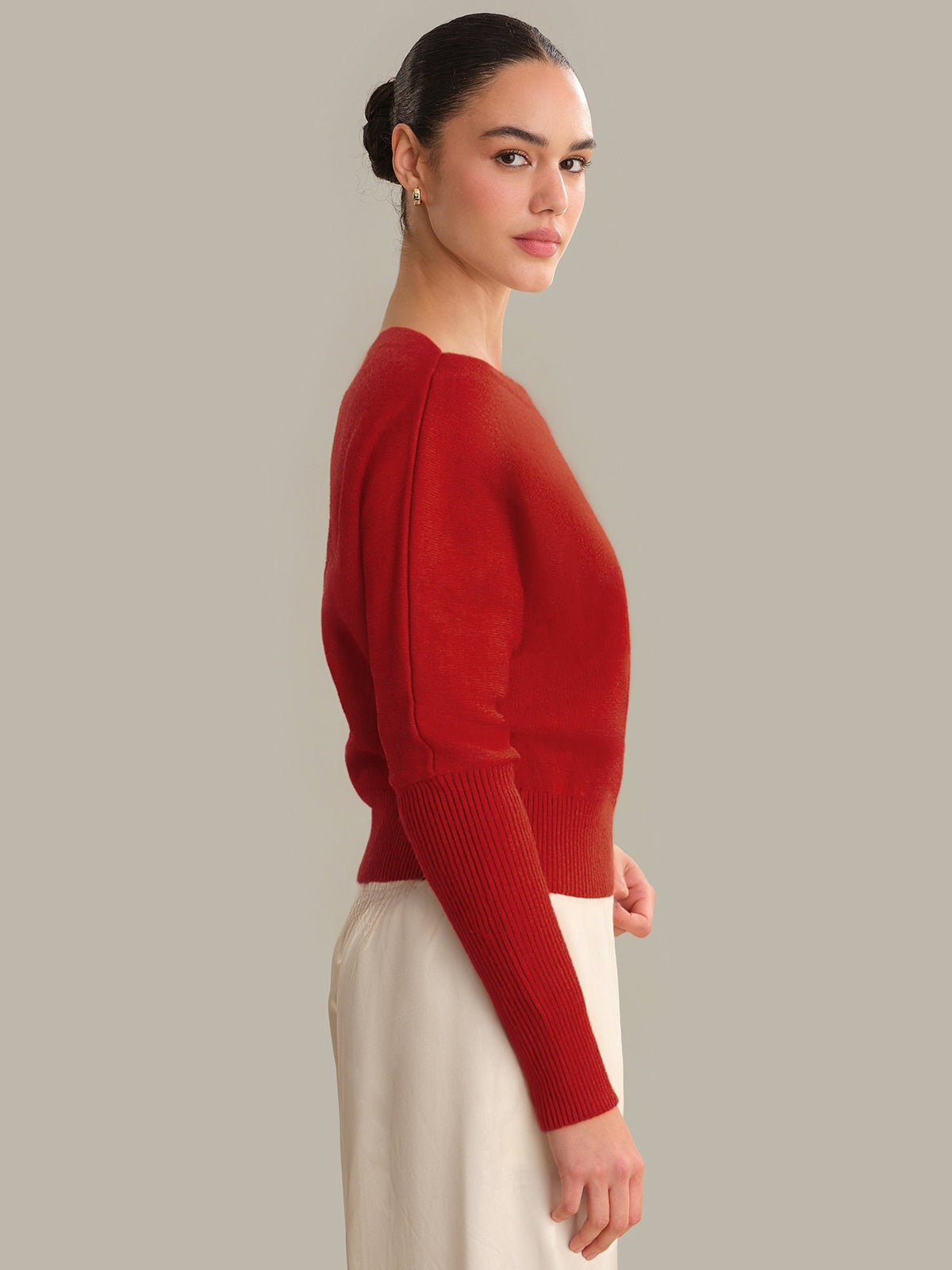 Woman wearing a red sweater and white pants against a gray background