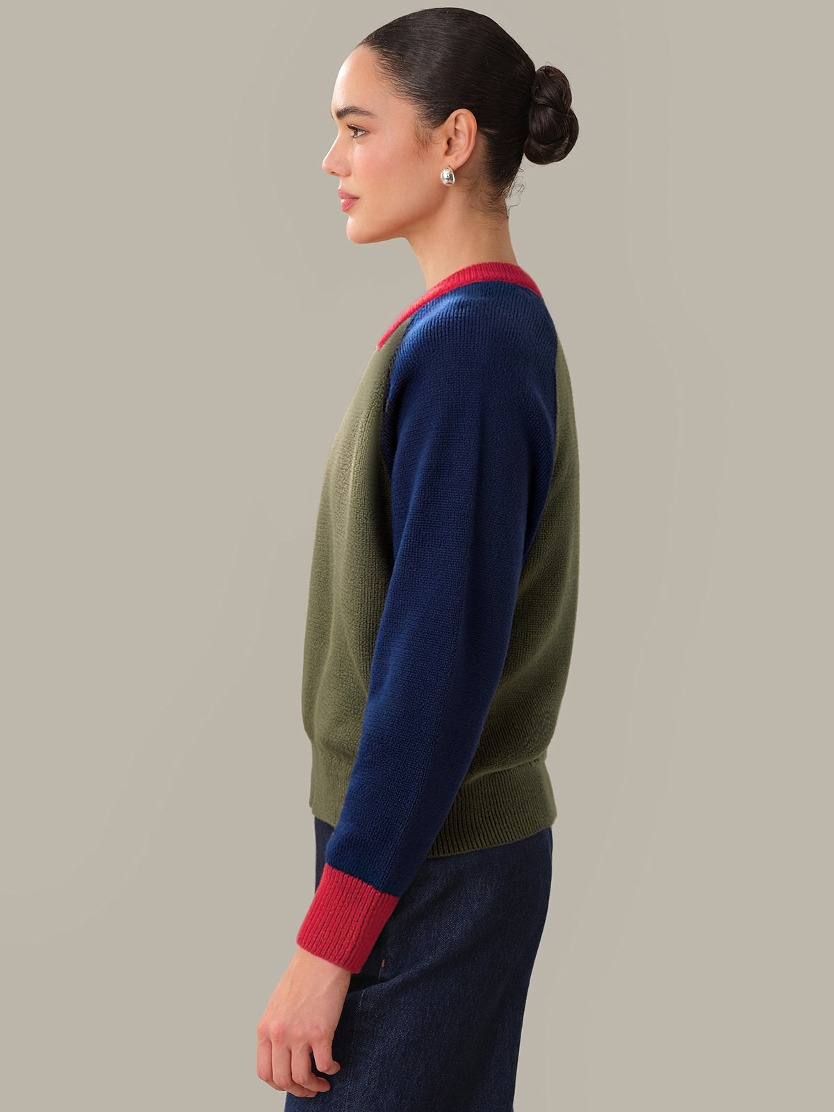 Woman wearing a green and navy sweater with red accents on a plain background