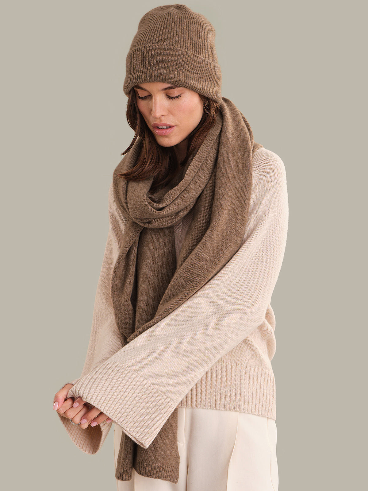 Woman wearing a beige knit hat and scarf with a beige sweater on a gray background