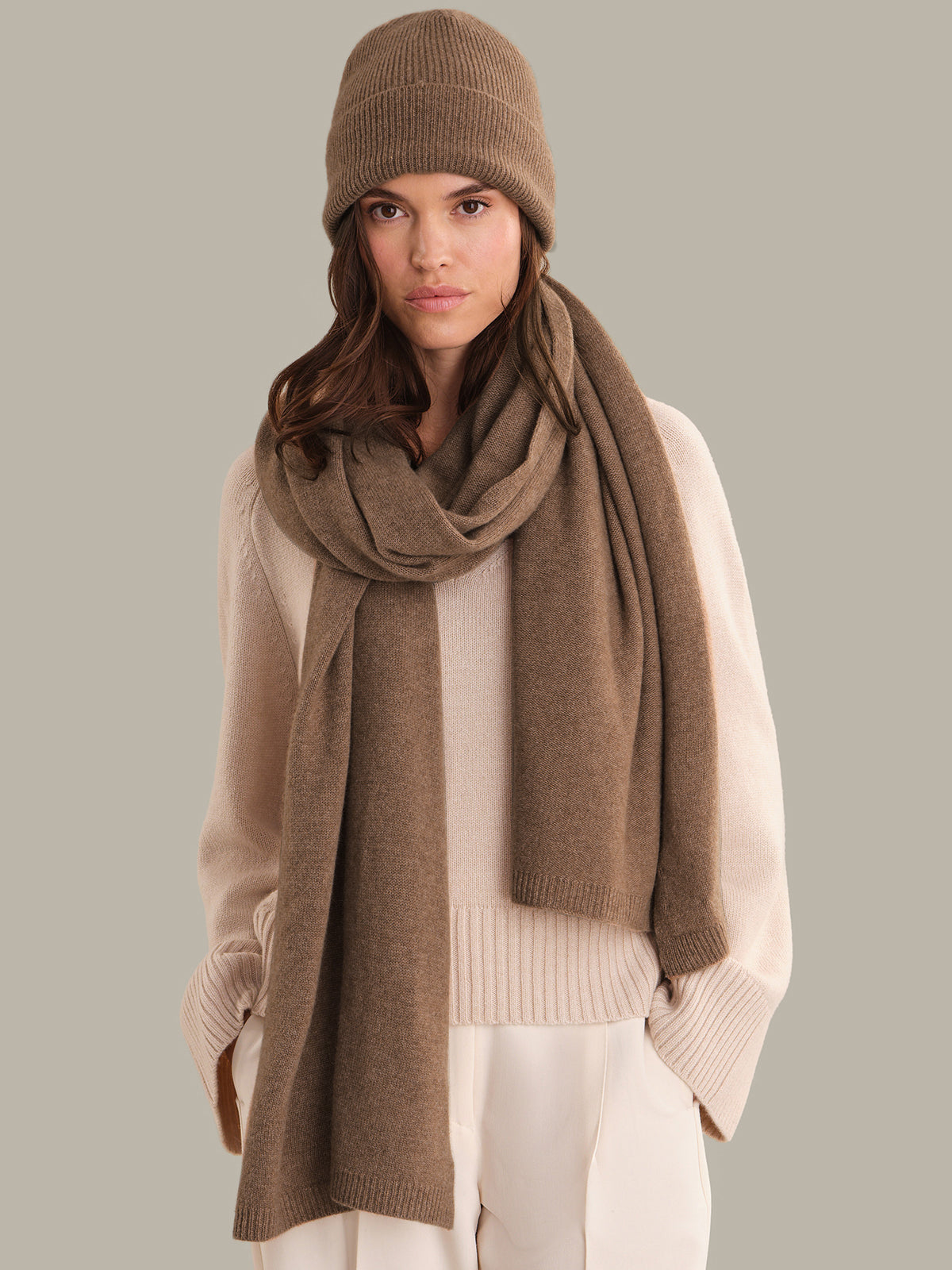 Woman wearing a brown knit hat and scarf on a plain background