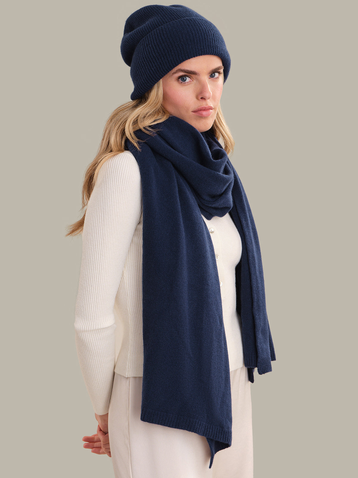 Woman wearing a navy blue knit hat and scarf on a plain background