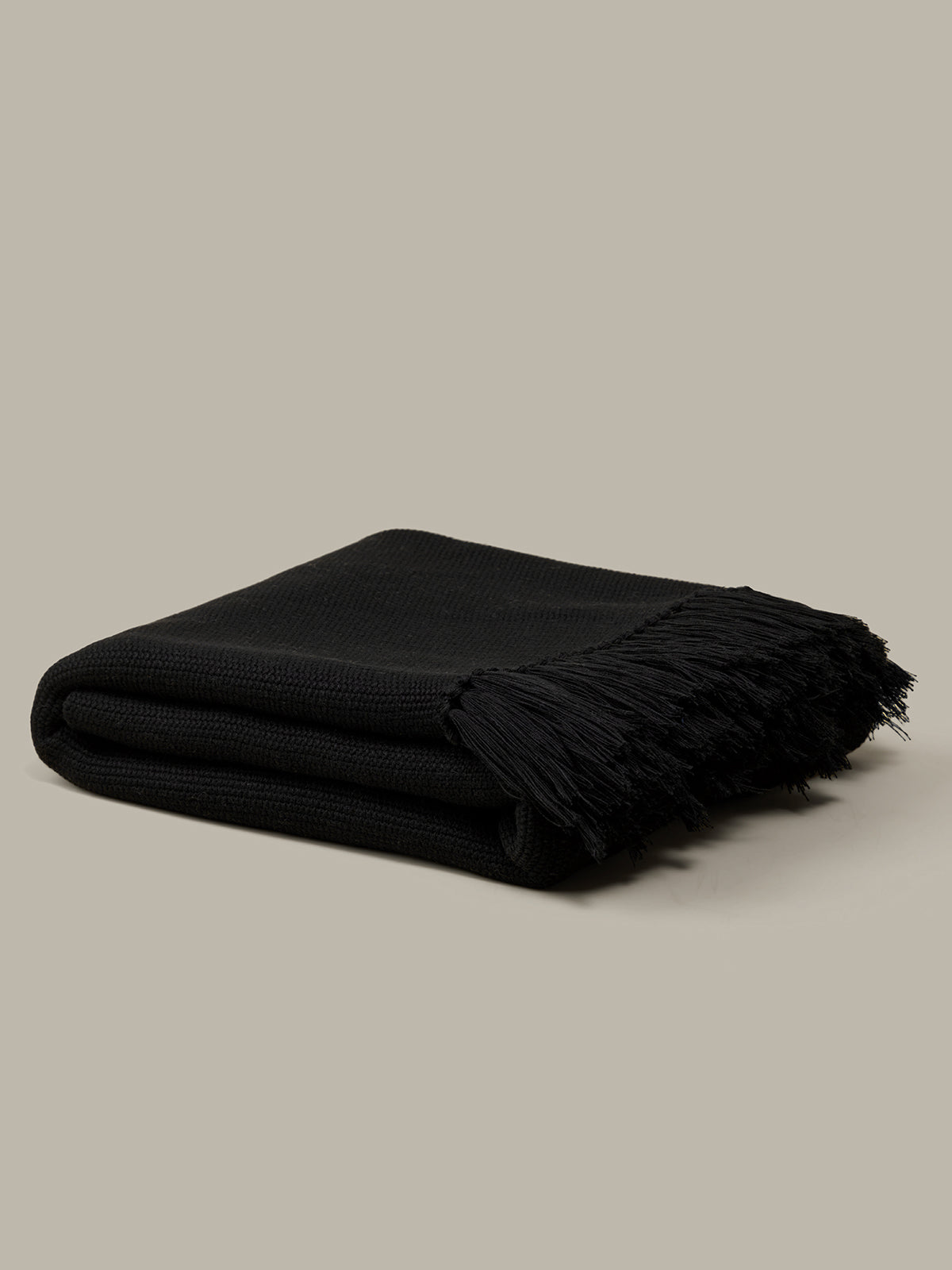 Folded black blanket with fringes on a beige background