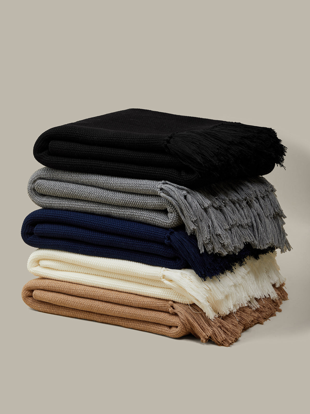Stack of folded blankets in black, gray, navy, white, and brown on a beige background