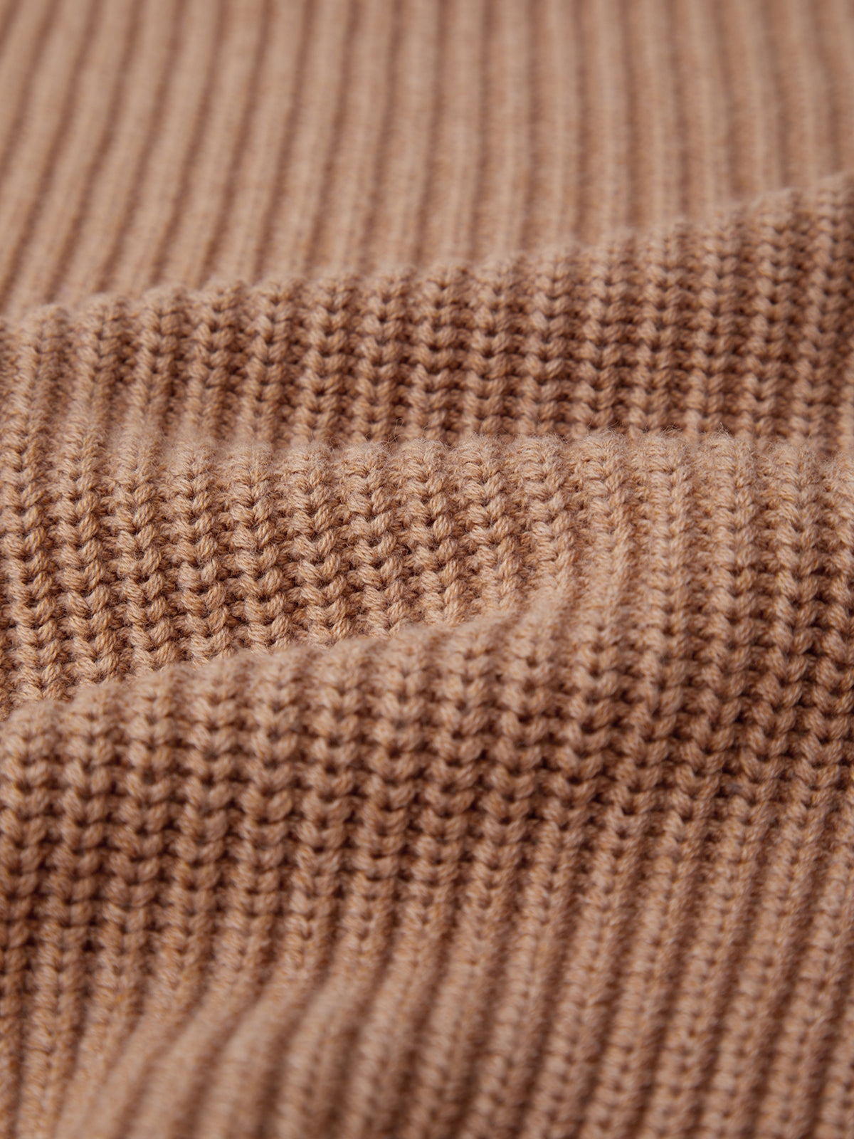 Close-up of the Jane: Crewneck Shaker Stitch Cotton Sweater in beige, highlighting its ribbed texture creating vertical lines. The soft cotton material looks cozy, with elegant folds casting gentle shadows across its fitted silhouette.