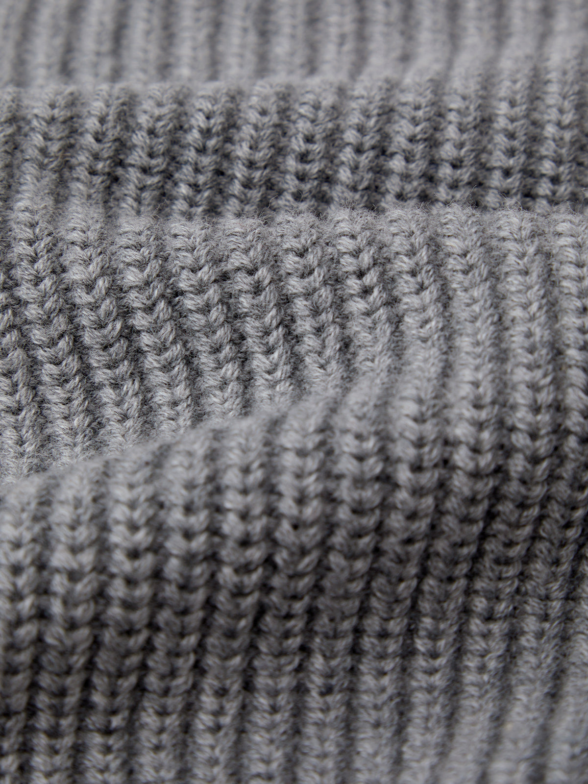 Close-up of a knitted fabric with a ribbed pattern. The gray texture features uniform rows, similar to the 525 Americas Ava V-Neck Sweater shaker stitch design, creating raised and recessed lines typical of a 100% cotton sweater.