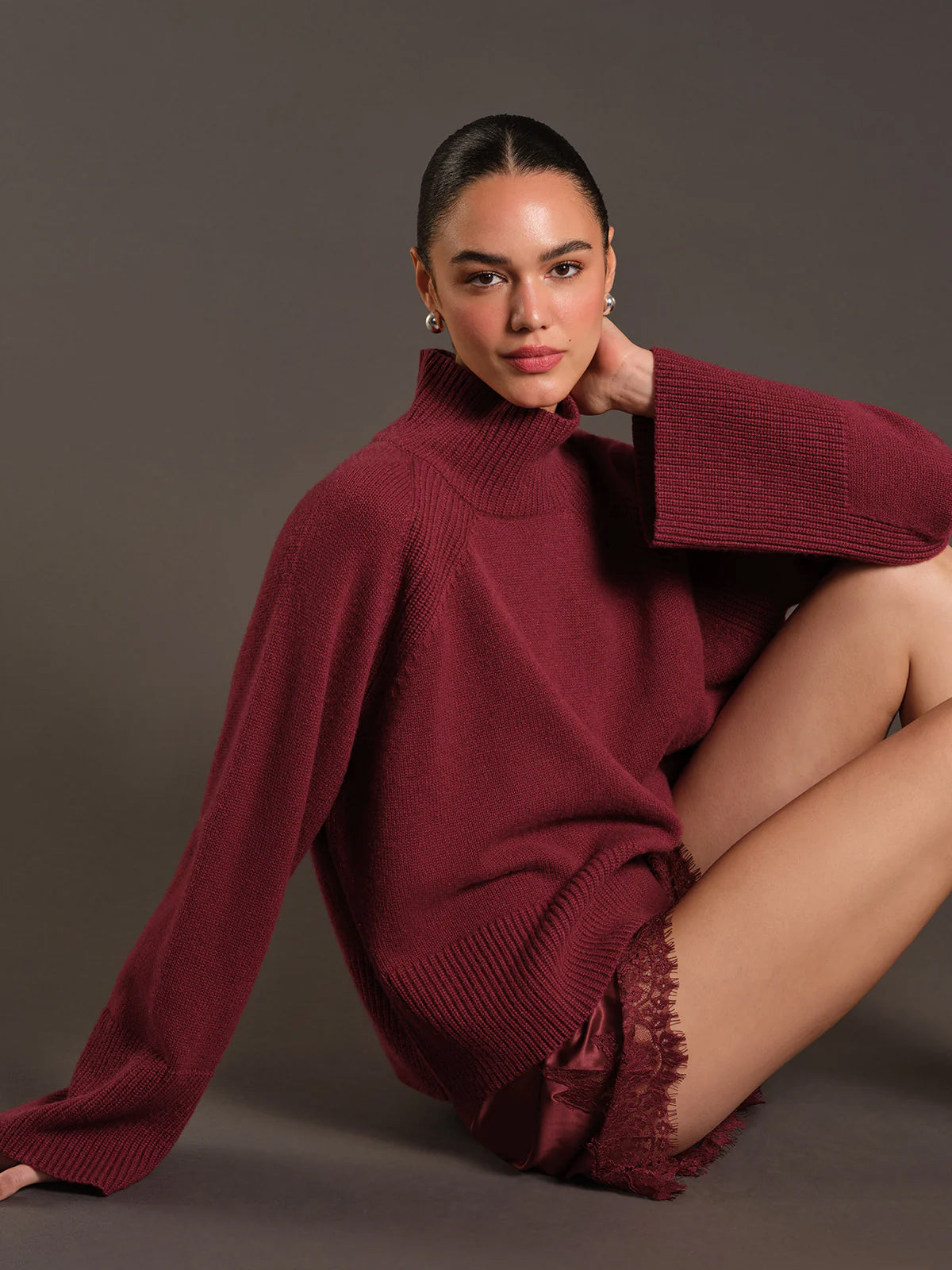 Woman wearing a burgundy sweater sitting on the floor against a gray background