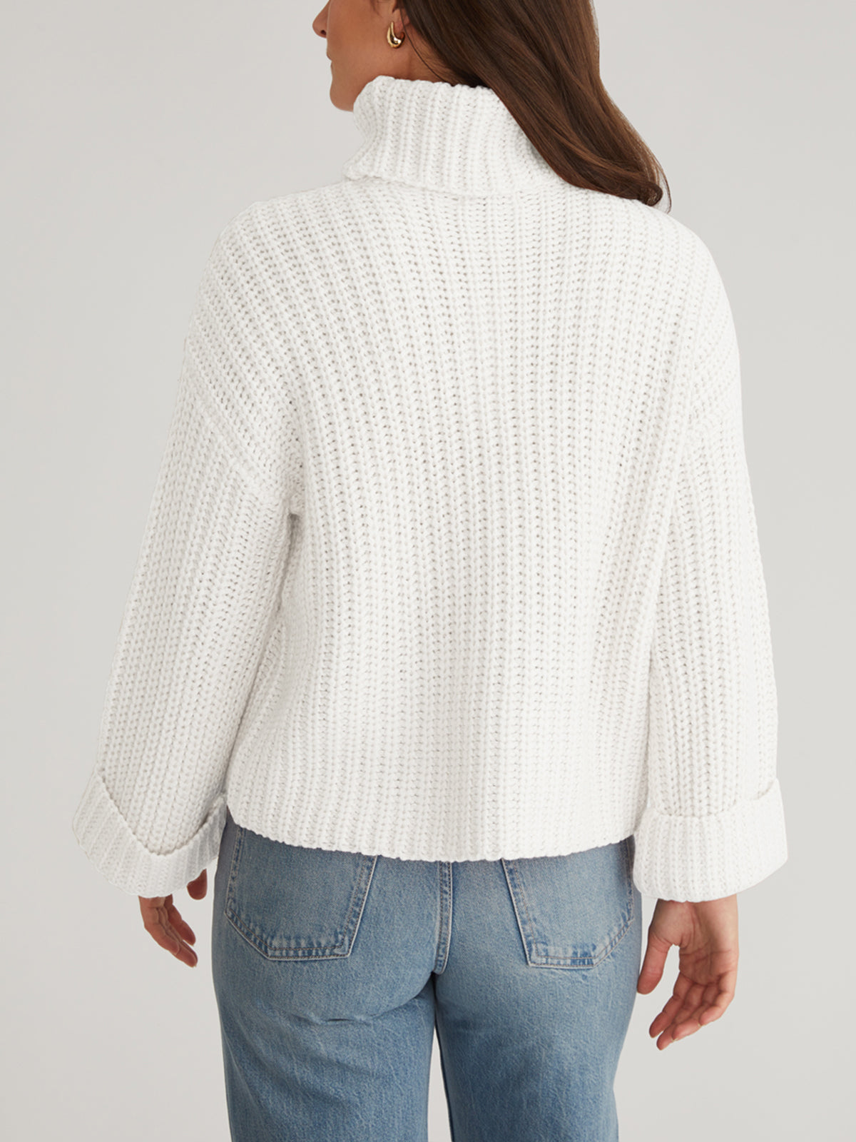 A person is shown from the back against a plain background, wearing 525 America’s chunky white Turtleneck Shaker Pullover with cozy turtleneck, cuffed oversized sleeves, and blue jeans.