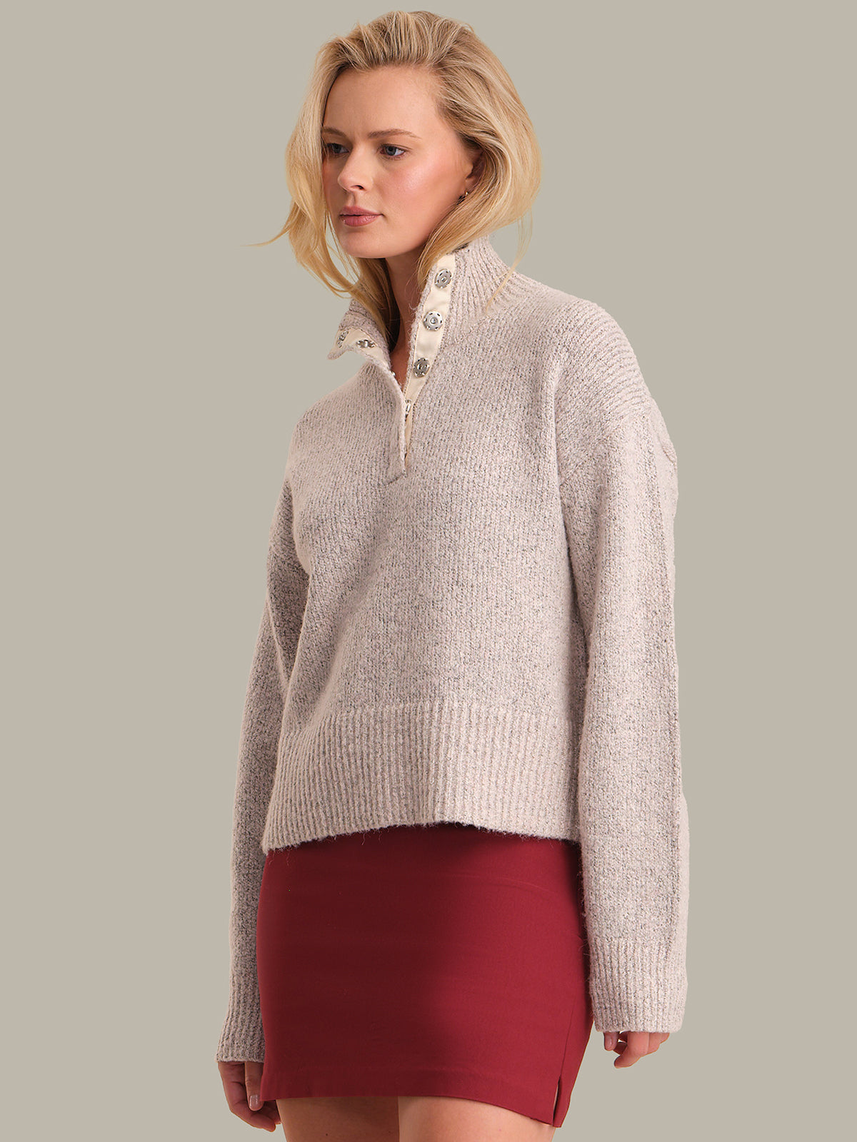 Woman wearing a beige knitted sweater with a high collar against a gray background