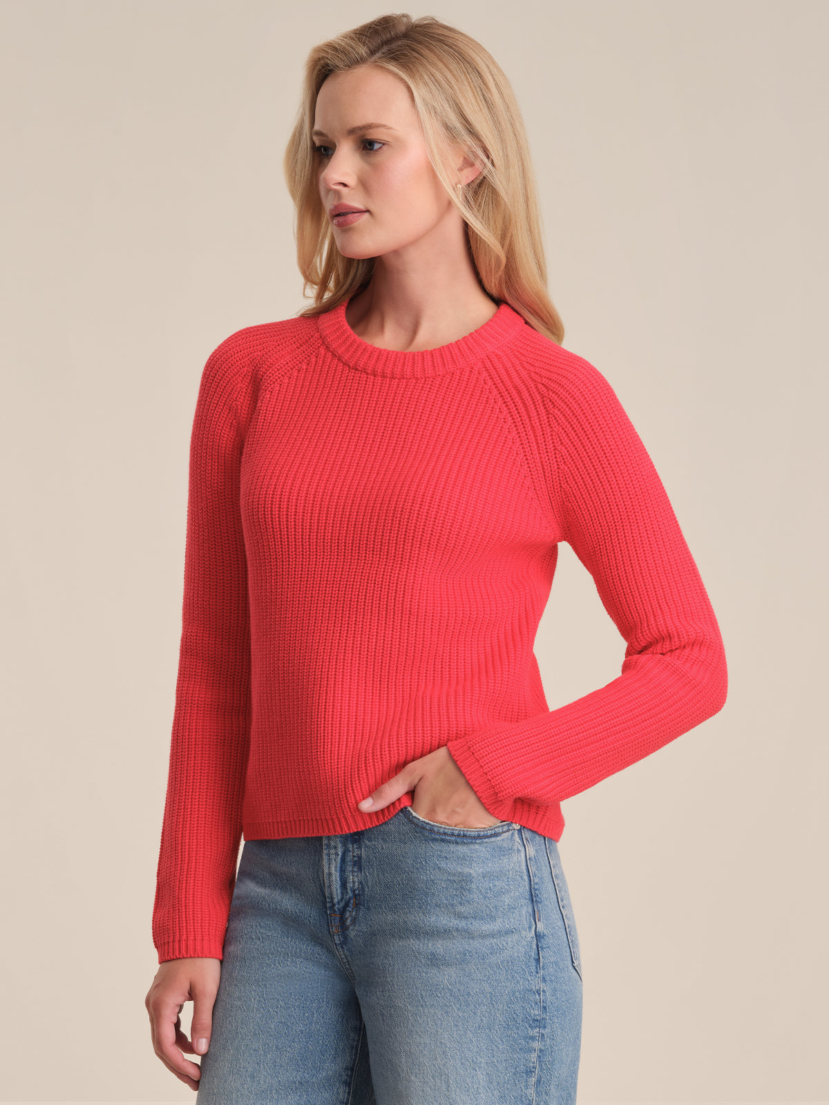 Wearing a bright red 525 America cotton shaker stitch sweater with a fitted silhouette and light blue jeans, a person stands slightly to the side, one hand on their hip, against a simple light background.