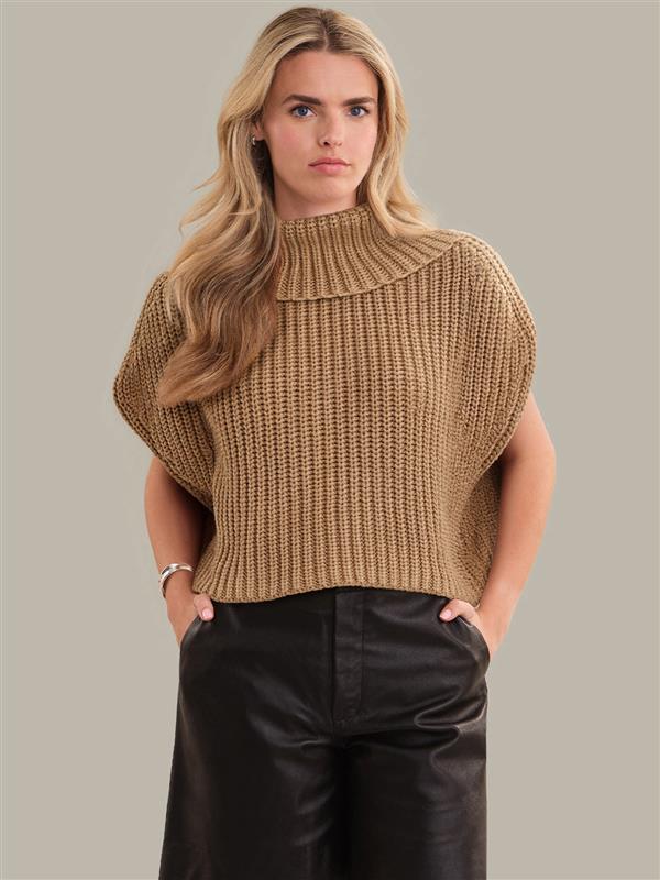 Woman wearing a beige knitted sleeveless sweater against a plain background