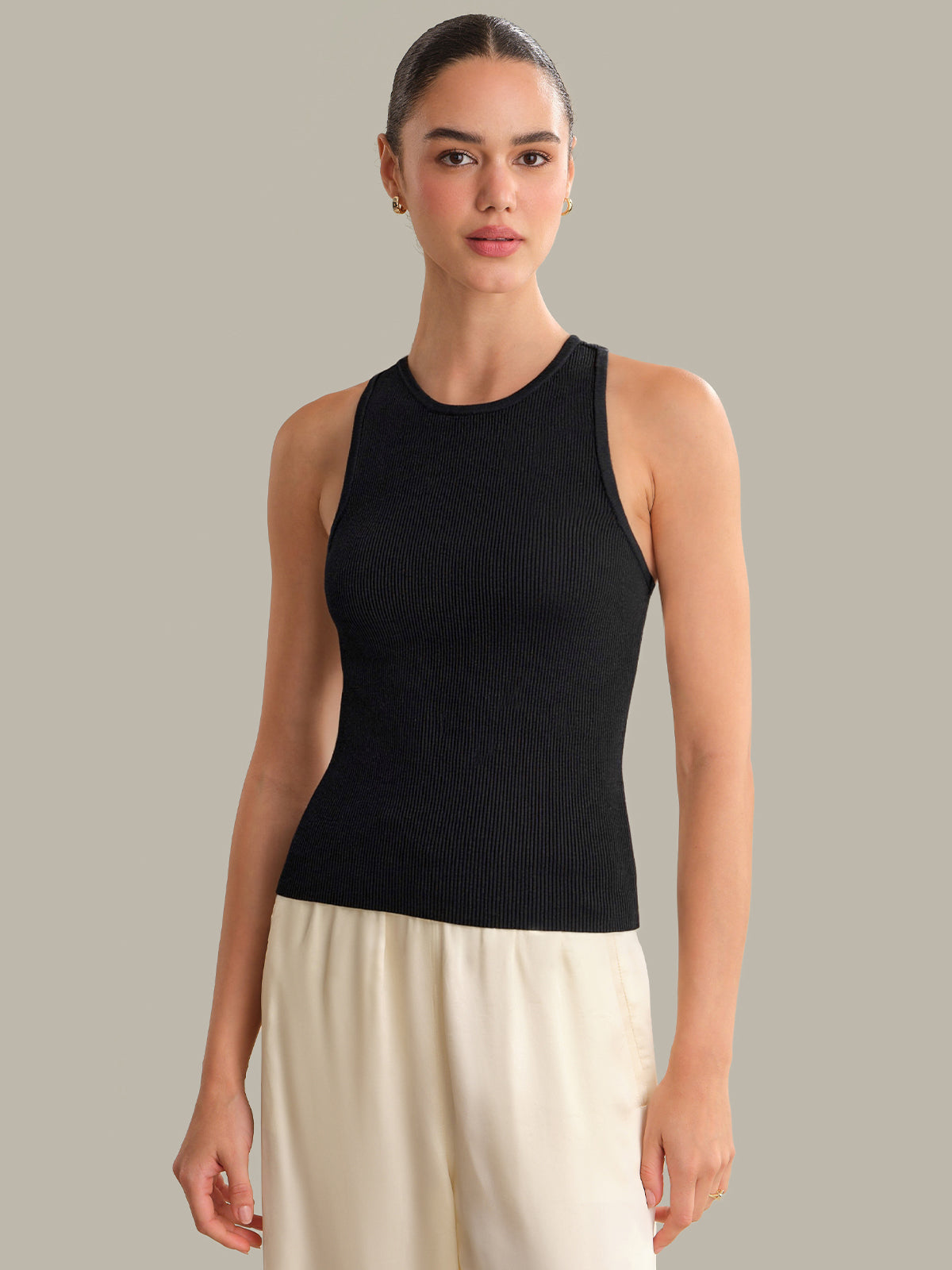 Woman wearing a black sleeveless top and beige pants against a neutral background