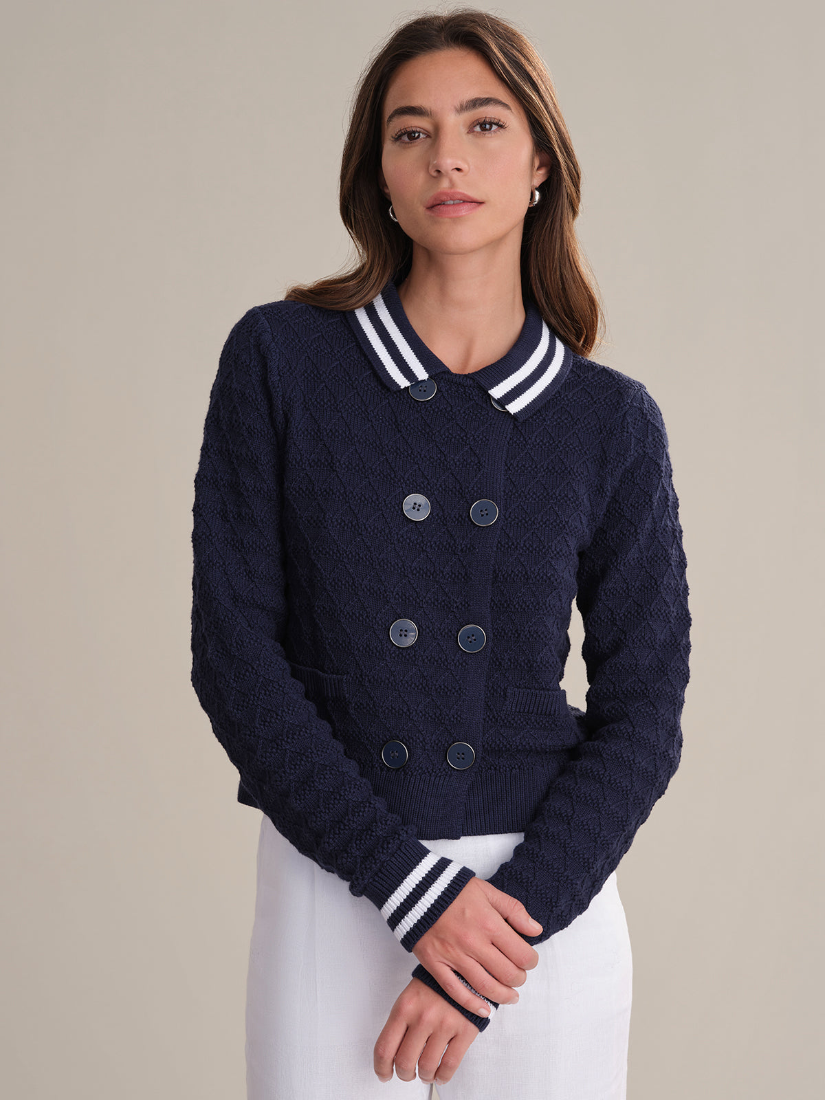 A woman wears a 525 America navy blue textured button-up sweater with sailor-inspired striped collar and cuffs, paired with a white skirt, standing against a plain beige background.