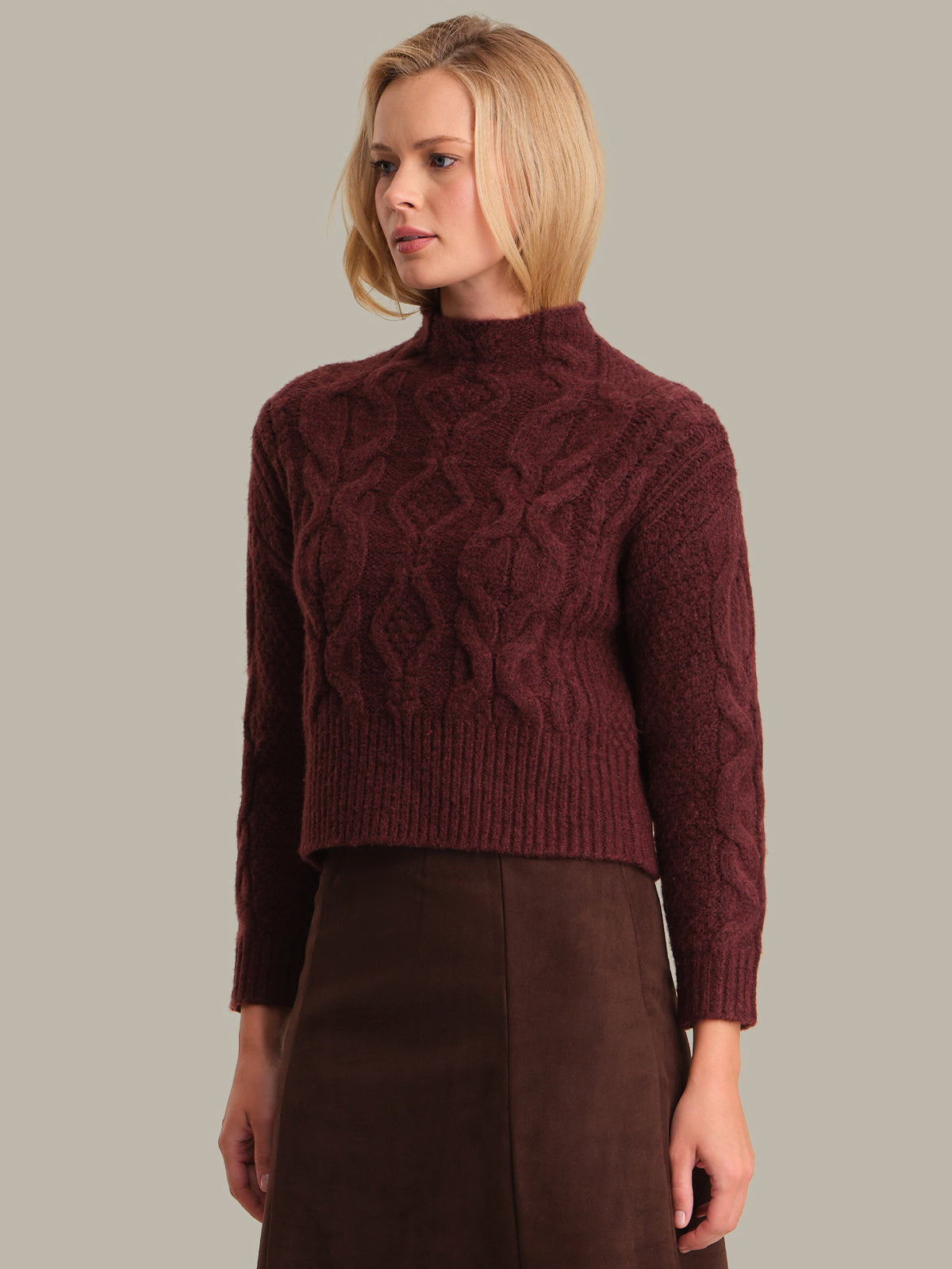 Woman wearing a maroon cable knit sweater against a plain background