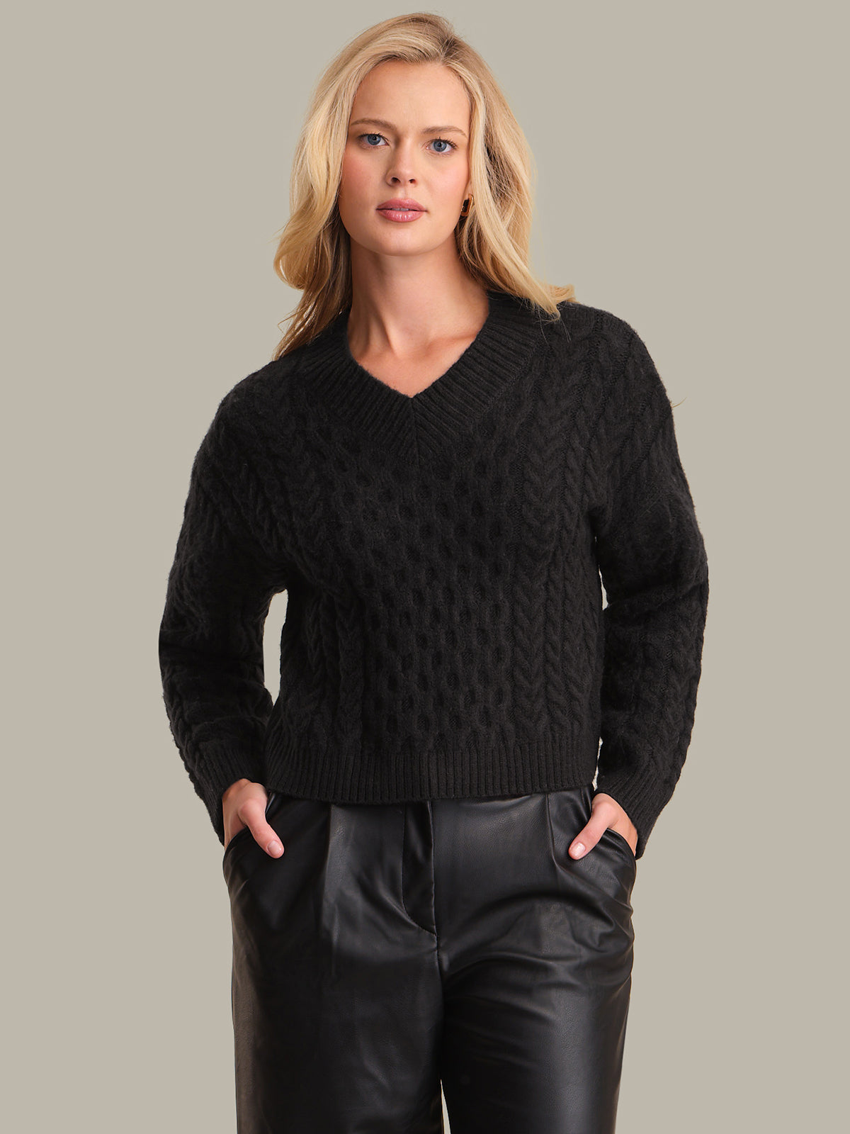 Woman wearing a black cable knit sweater against a neutral background