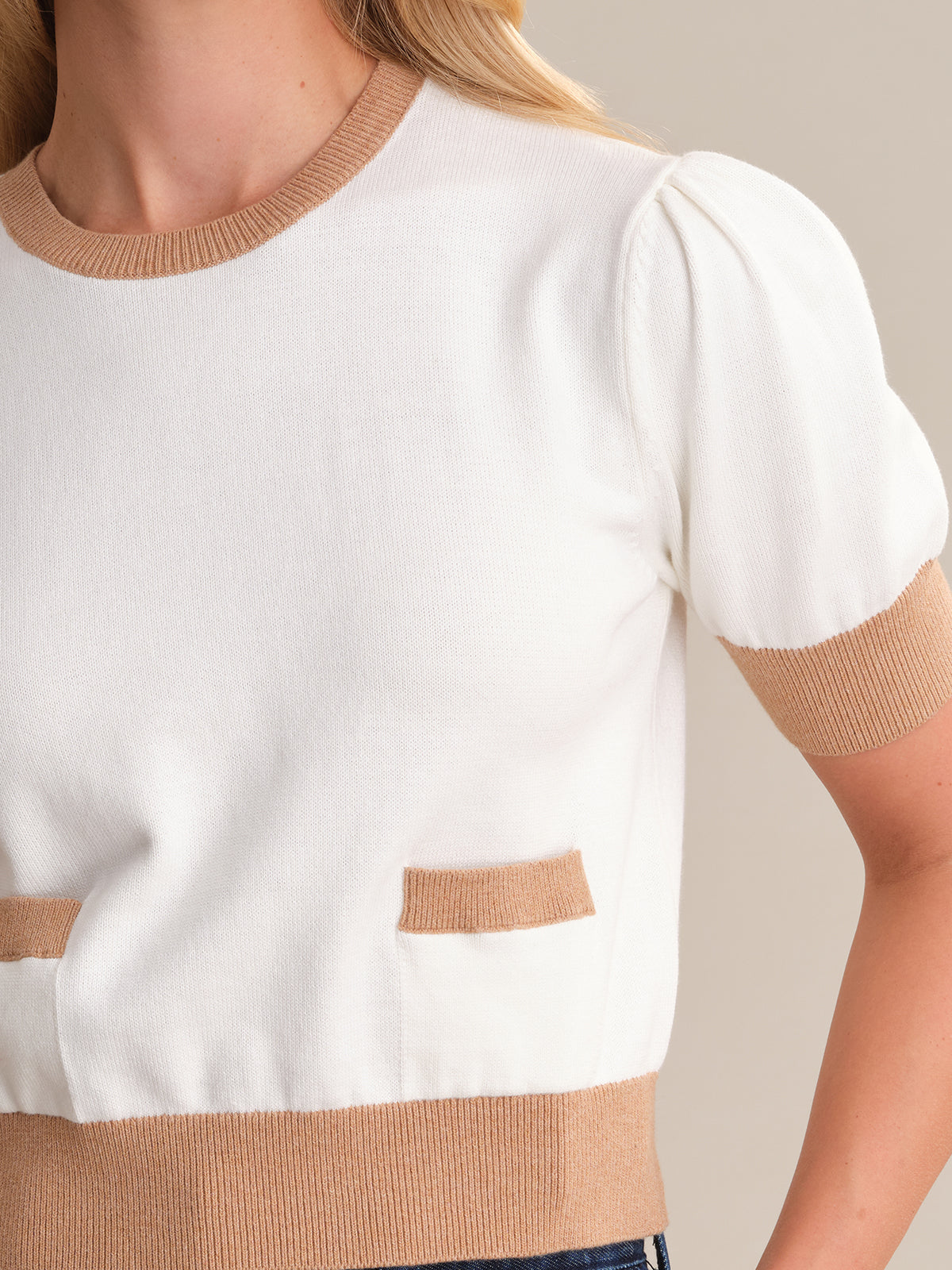 A person is wearing a 525 America feminine pullover with white short sleeves and light brown trim on the neckline, cuffs, and waist. Its made from 100% cotton, has two small front pockets, and is set against a neutral beige background.