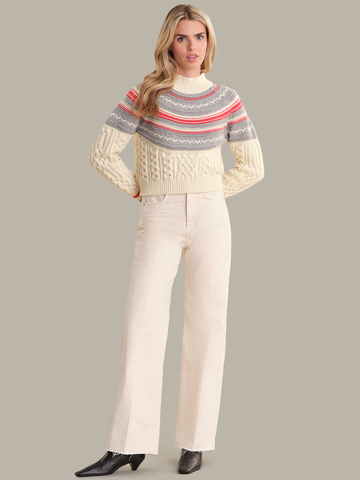 Woman wearing a patterned sweater and white pants on a gray background