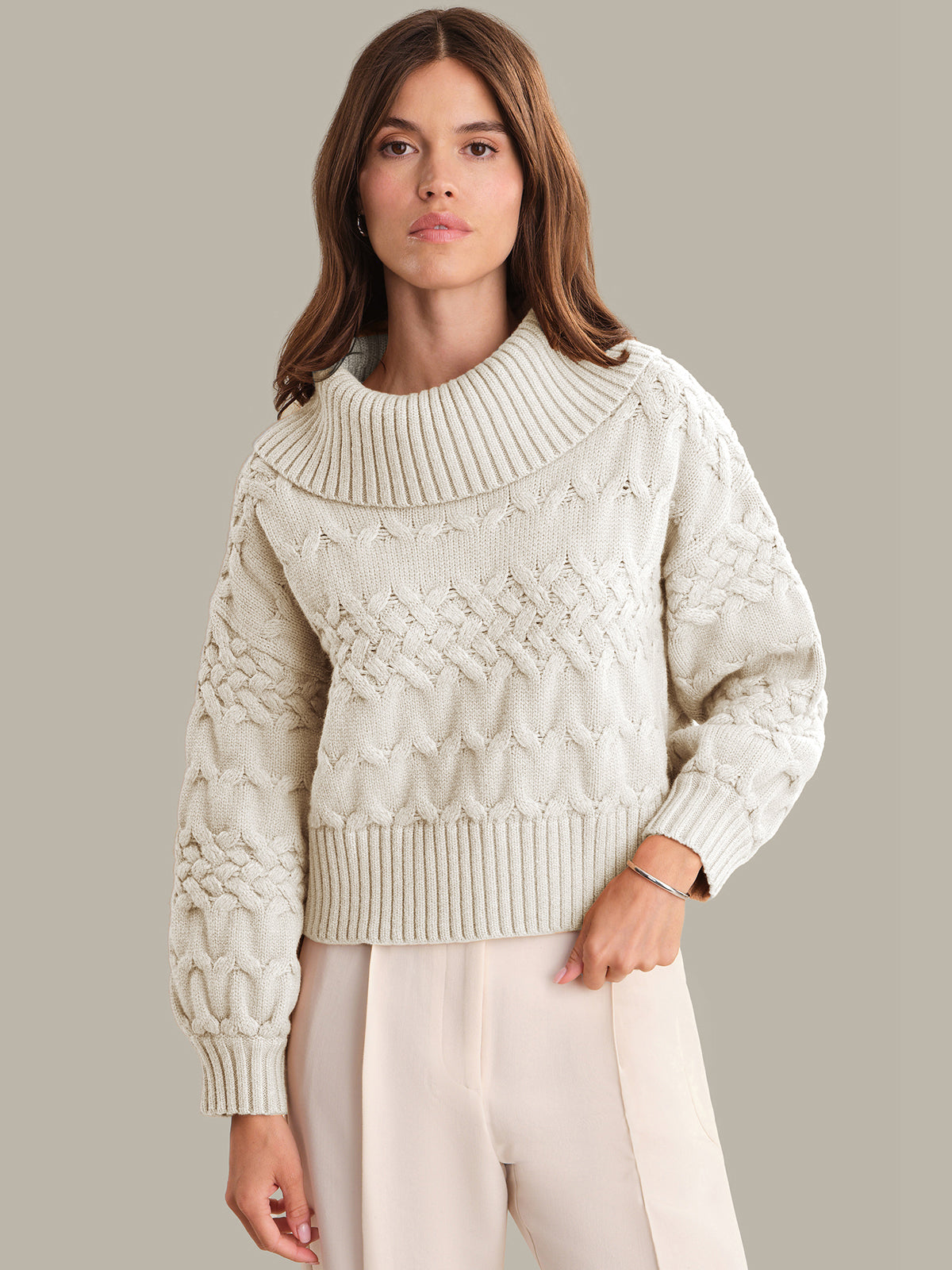 Woman wearing a cream-colored cable knit sweater against a neutral background