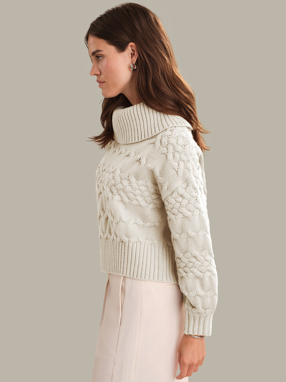 Woman wearing a cream knitted sweater against a plain background