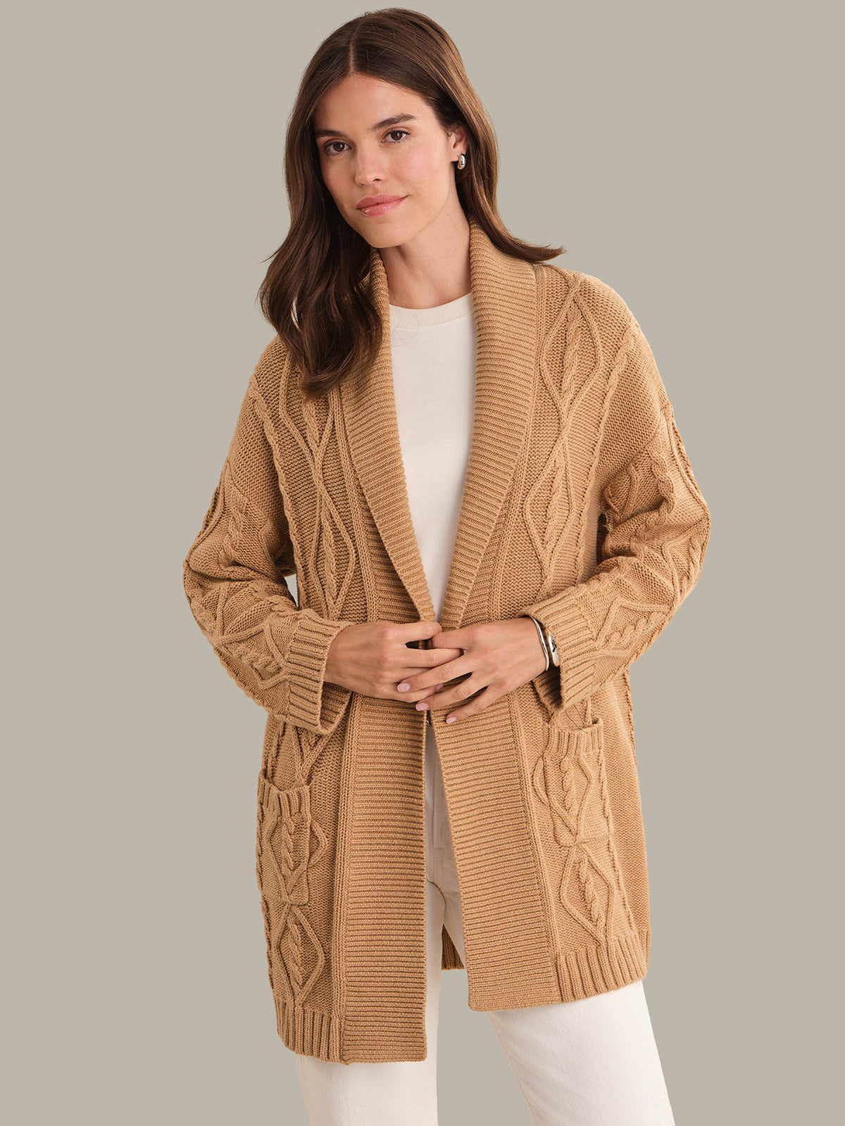 Woman wearing a beige cable knit cardigan against a plain background