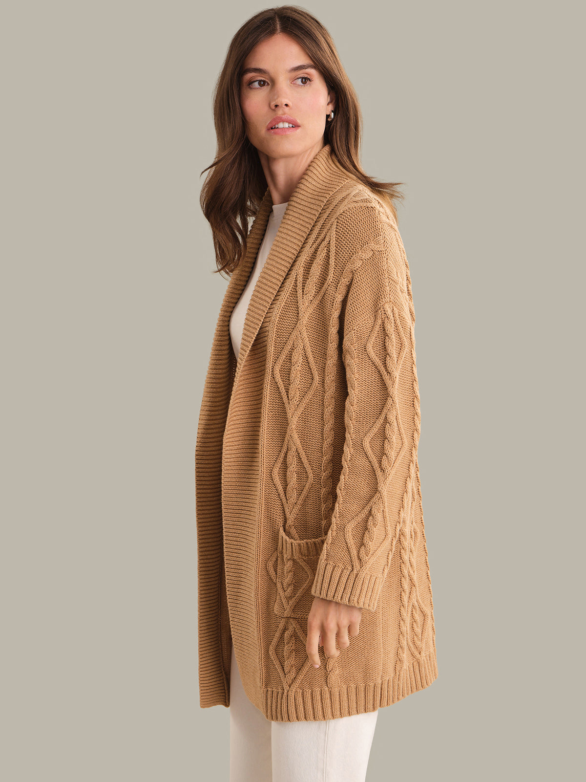 Woman wearing a long beige knitted cardigan on a plain background