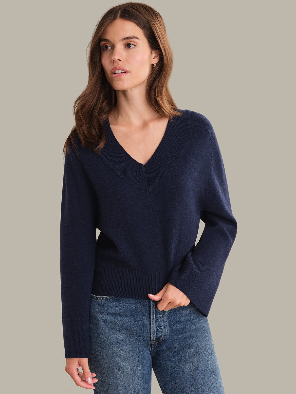 Woman wearing a navy sweater and blue jeans against a neutral background