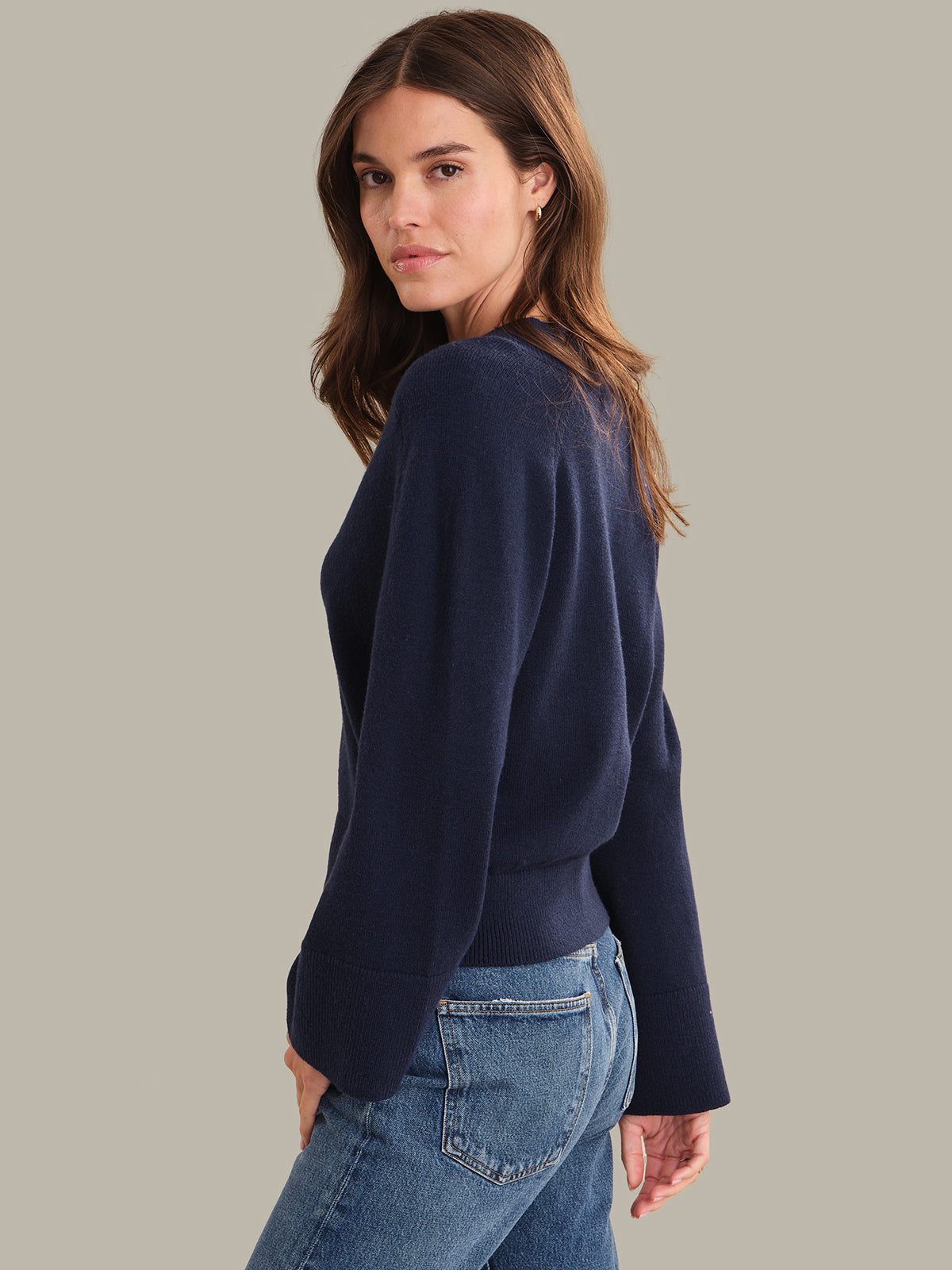 Woman wearing a navy sweater and blue jeans on a gray background