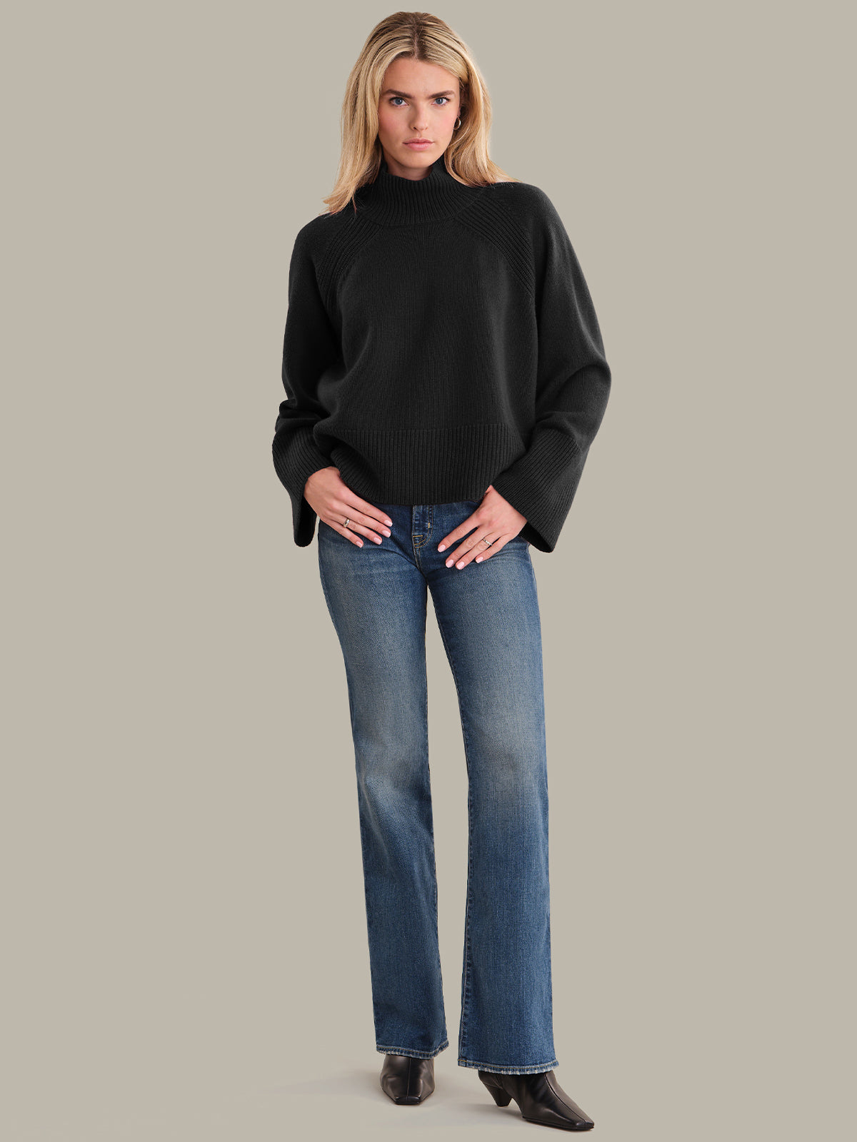 Woman wearing a black turtleneck sweater and blue jeans on a gray background