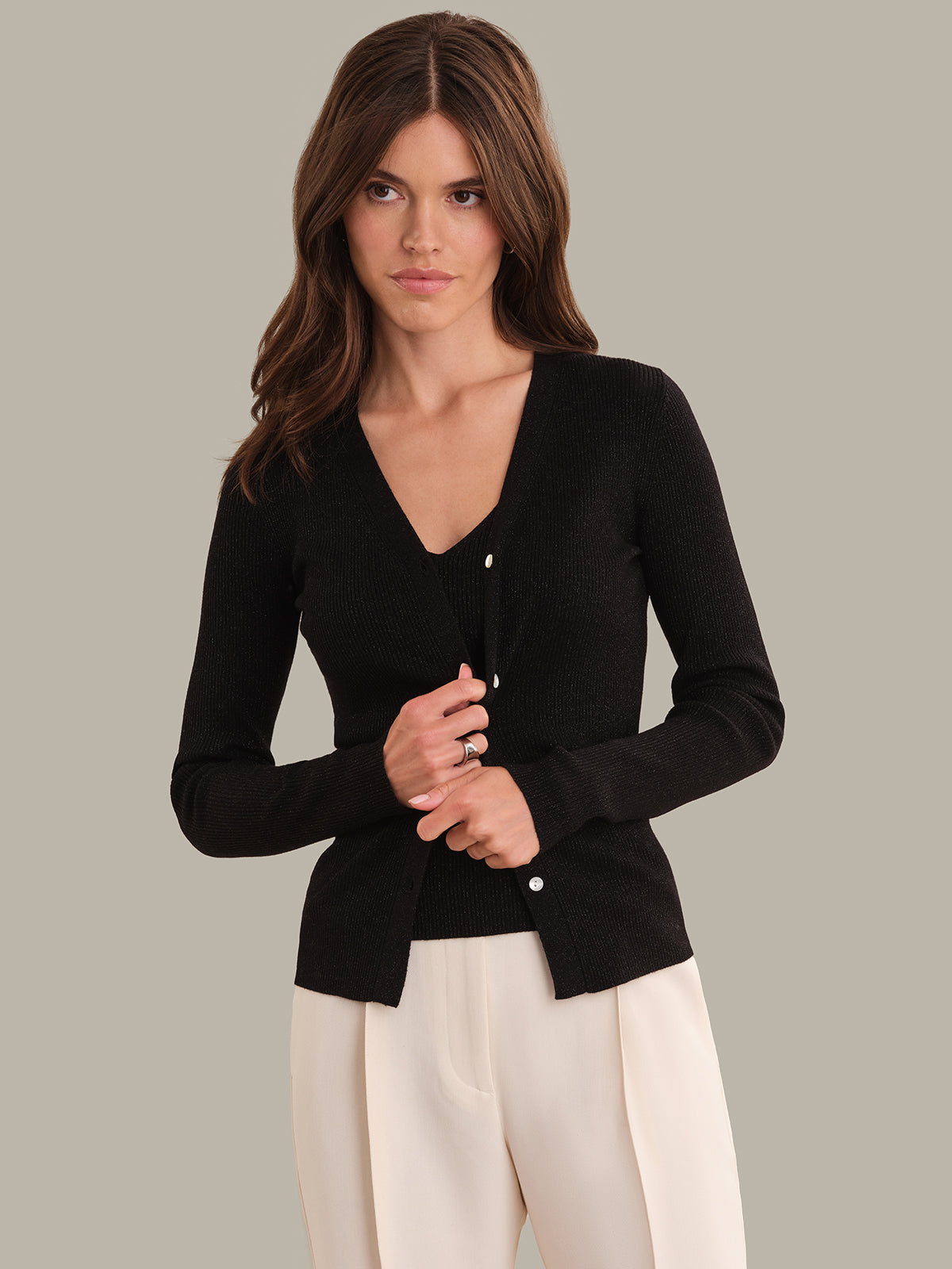 Woman wearing a black cardigan over a white top against a neutral background