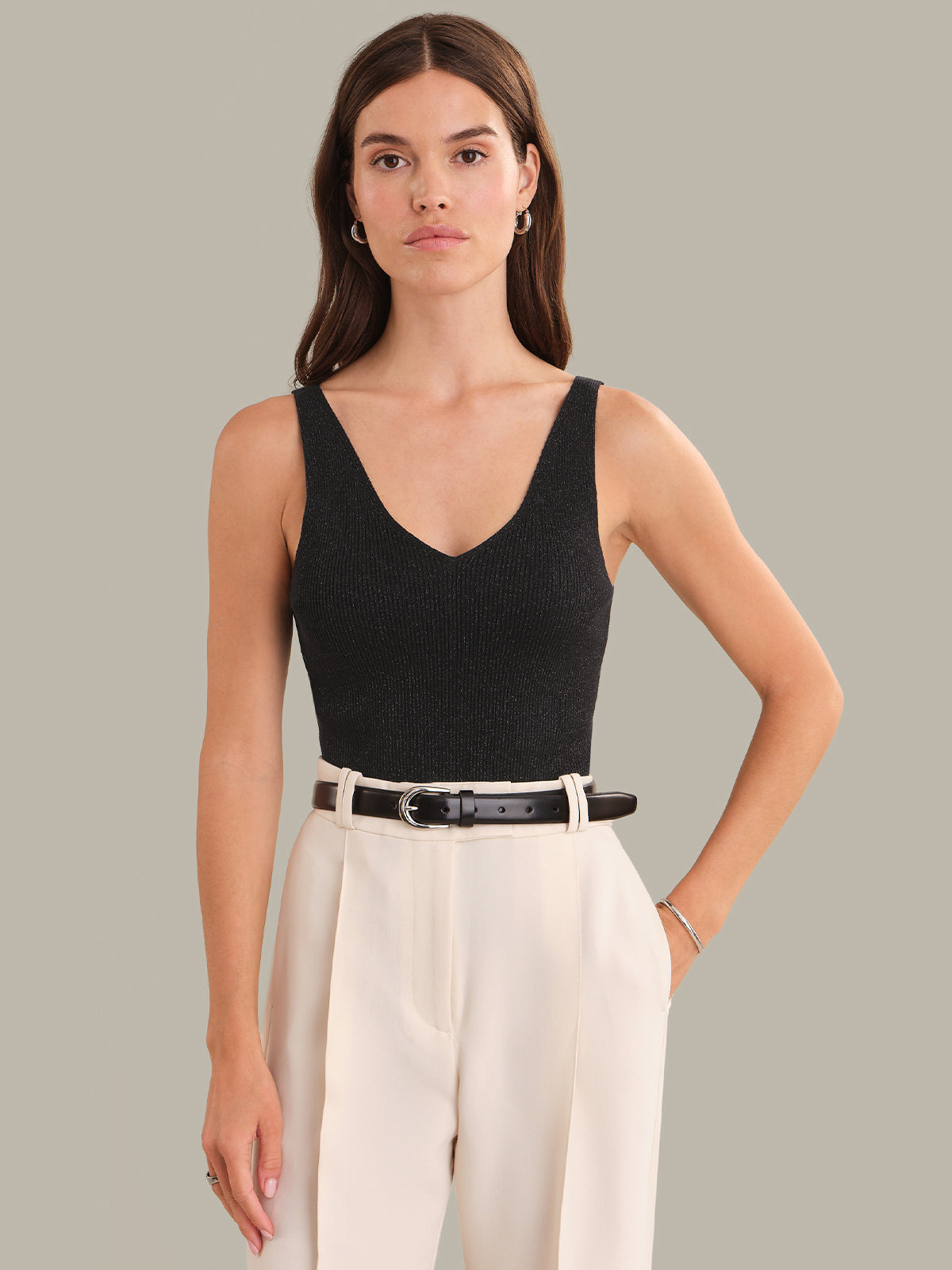 Woman wearing a black tank top and beige pants against a gray background