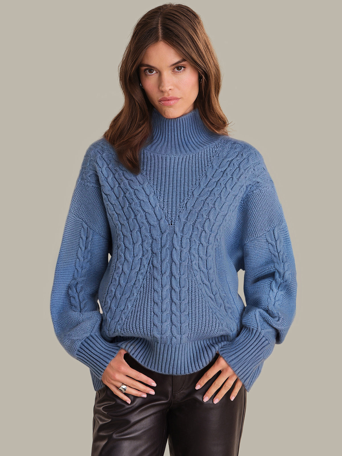 Woman wearing a blue cable knit sweater against a neutral background