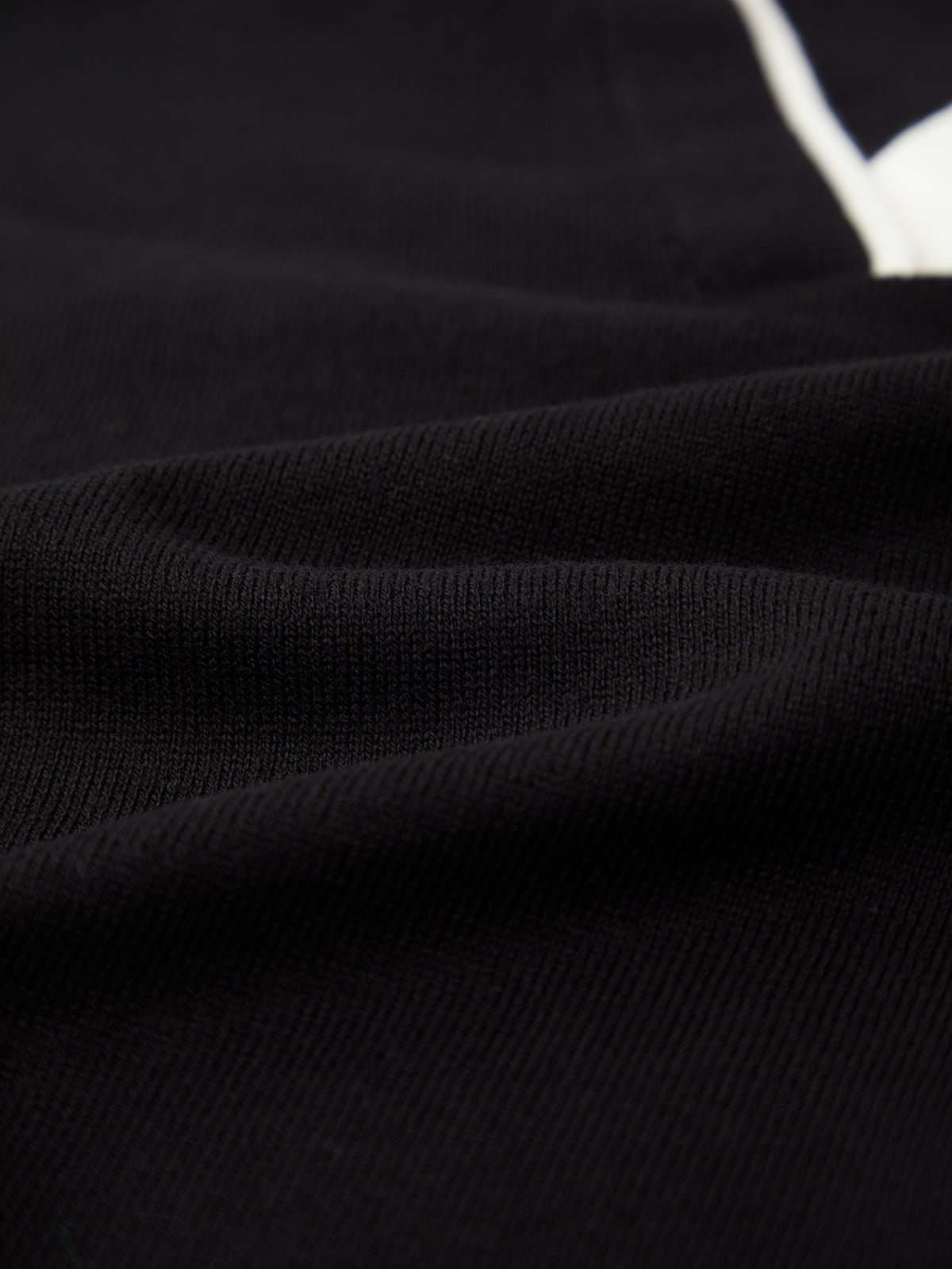 Close-up view of black breathable fabric with a textured surface and subtle folds, featuring a small white area in the upper right—ideal for a lightweight 525 America pullover.