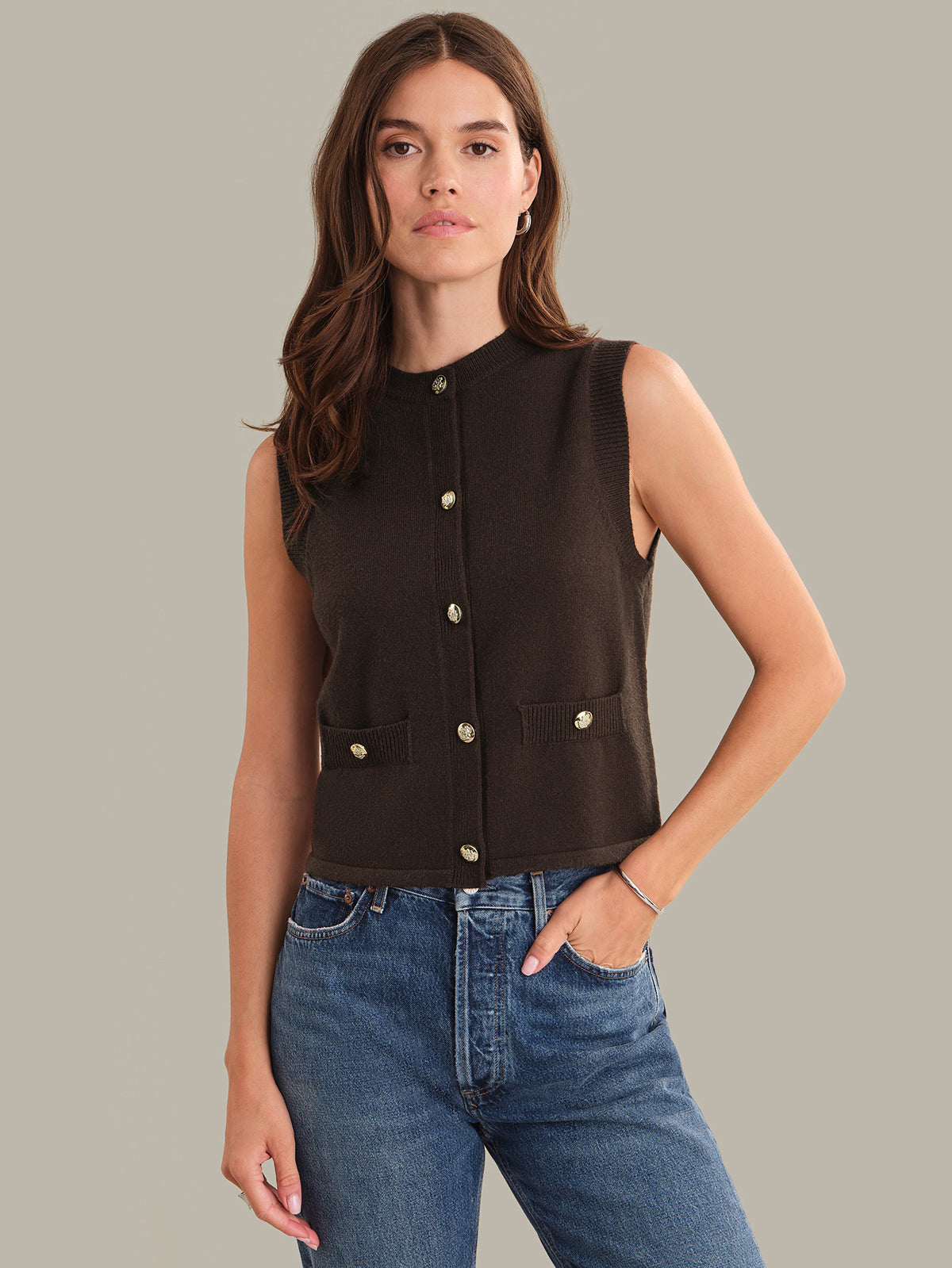 Woman wearing a shaved chocolate sleeveless button-up top with blue jeans on a neutral background