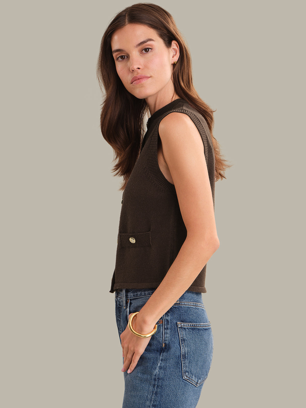 Woman wearing a shaved chocolate vest and blue jeans against a gray background