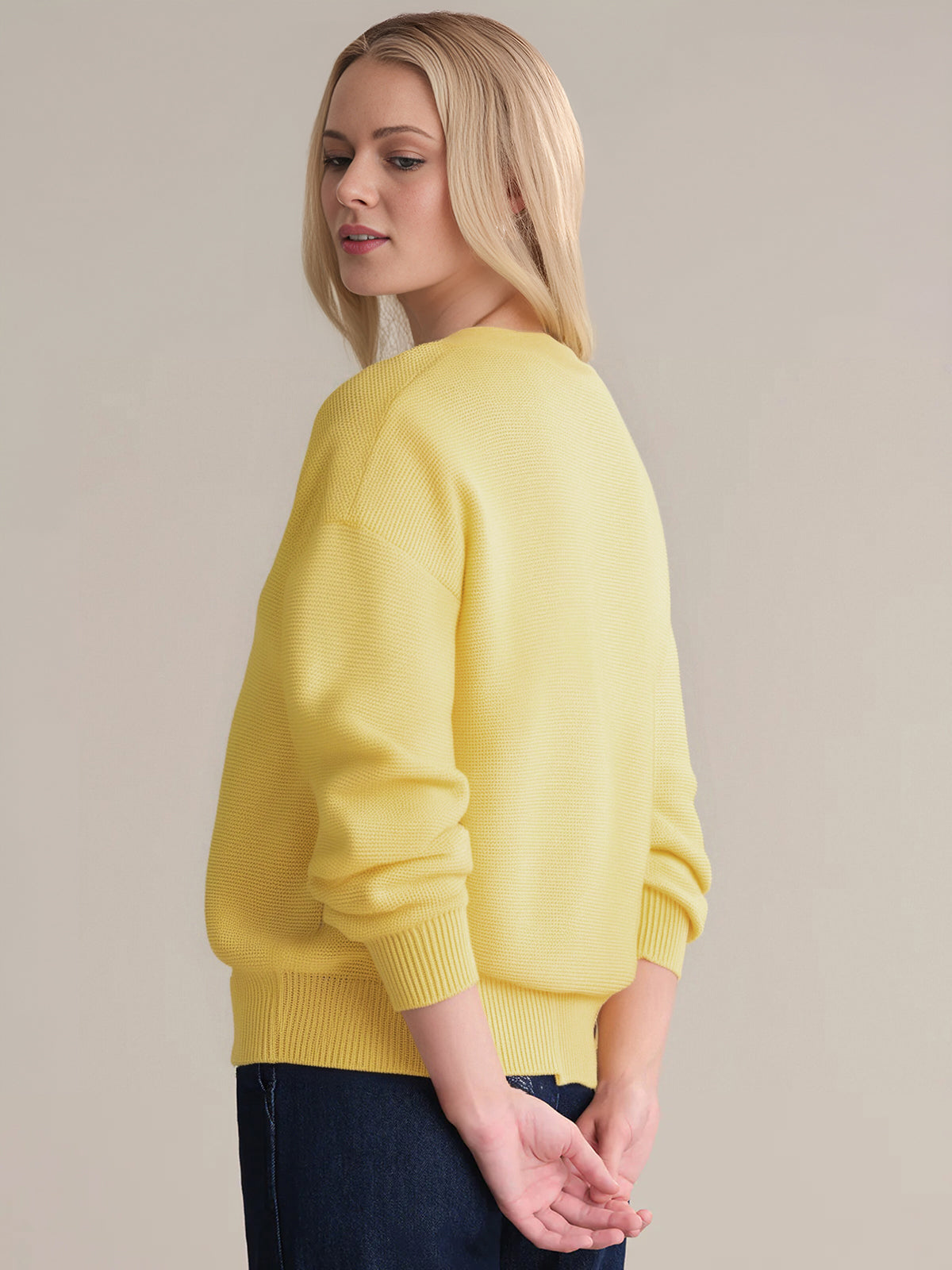 A person stands against a plain backdrop, wearing a 525 America lightweight yellow knit sweater with a classic crew neck and dark jeans—perfect for easy layering—with their head turned slightly and hands relaxed by their sides.