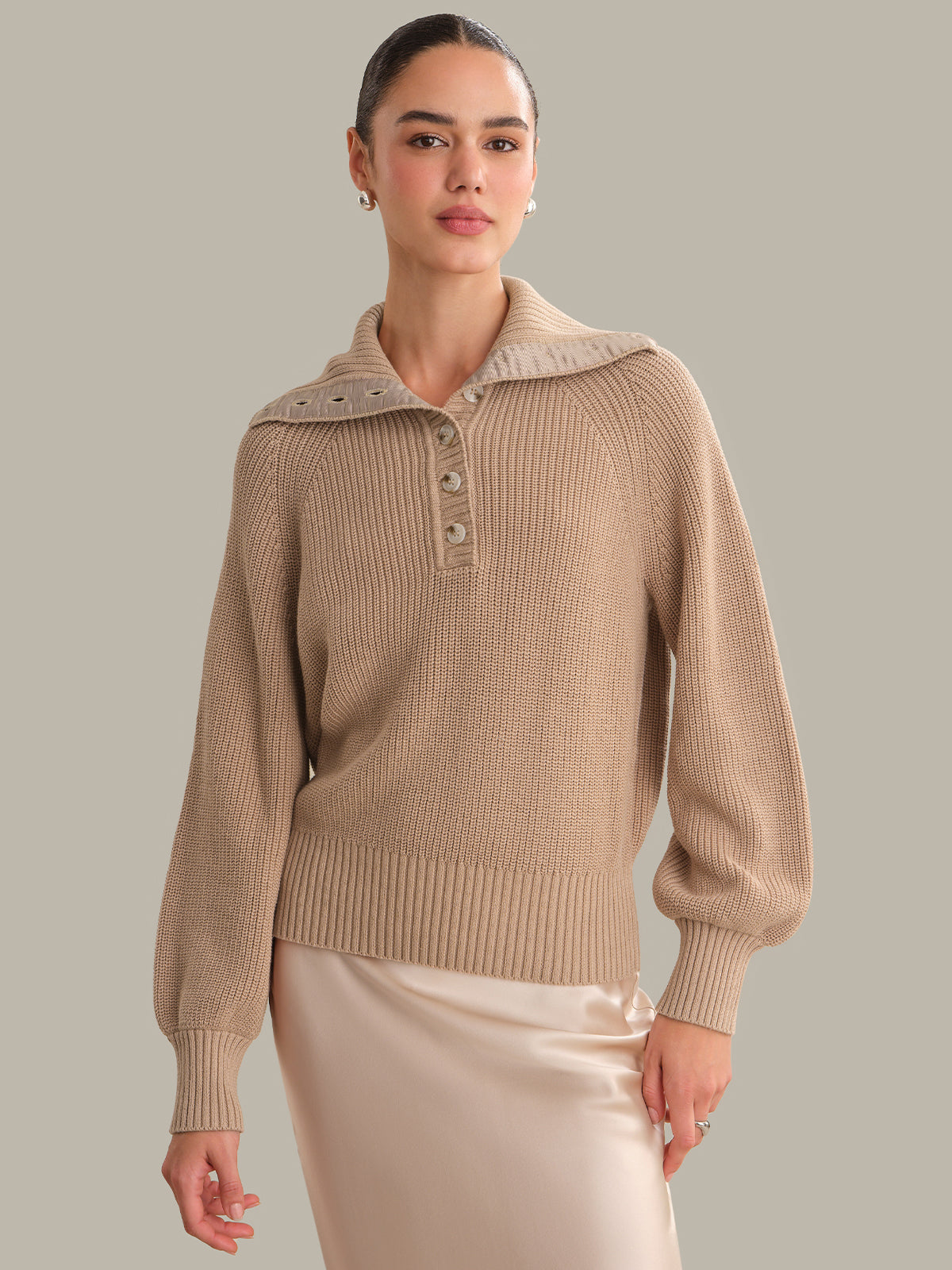 Woman wearing a beige sweater with a collar against a neutral background