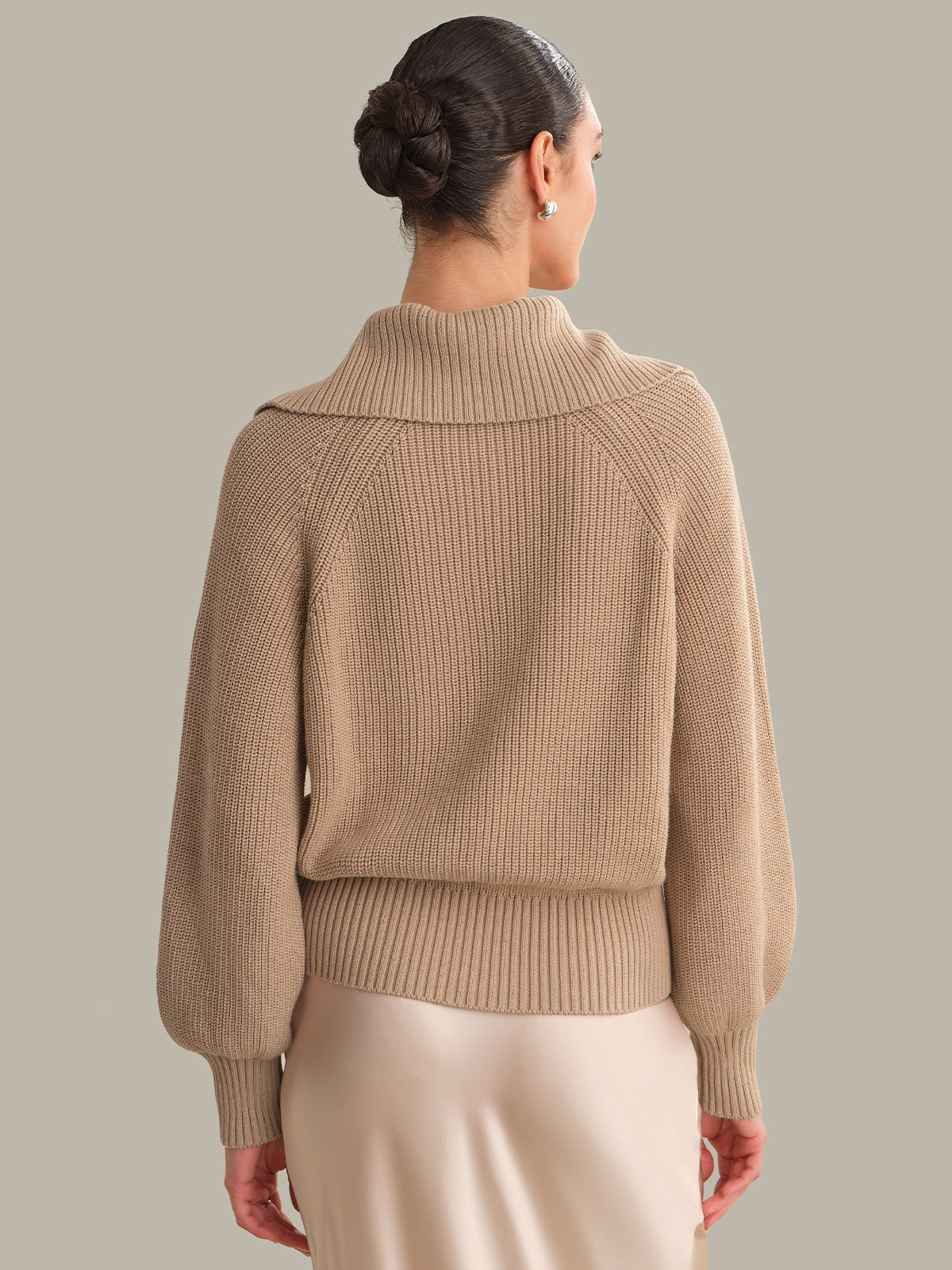 Woman wearing a beige knitted sweater against a neutral background