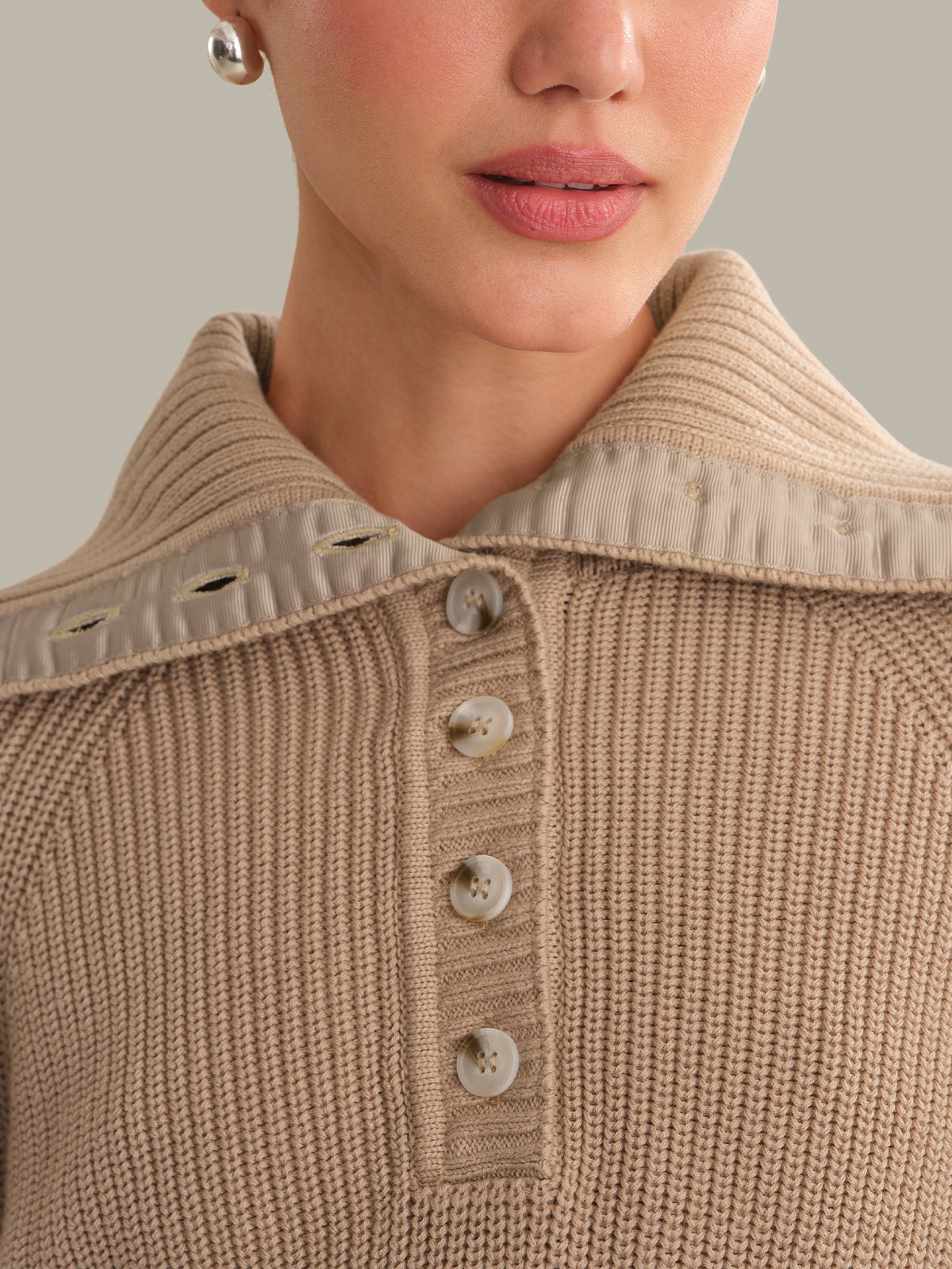 Close-up of a person wearing a beige knitted sweater with button details.