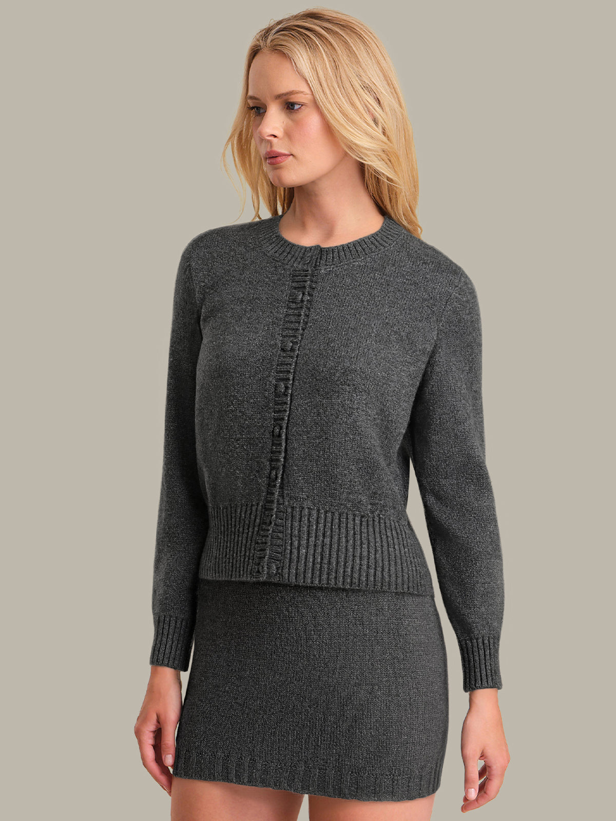 Woman wearing a gray knitted cardigan and skirt set against a neutral background