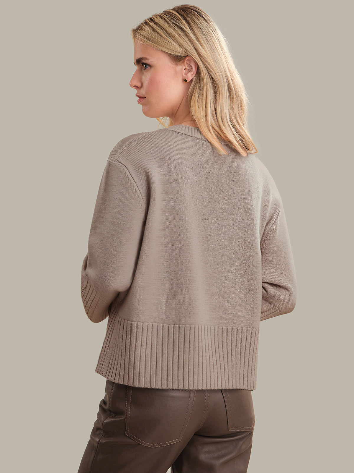Woman wearing a beige sweater and brown pants against a plain background