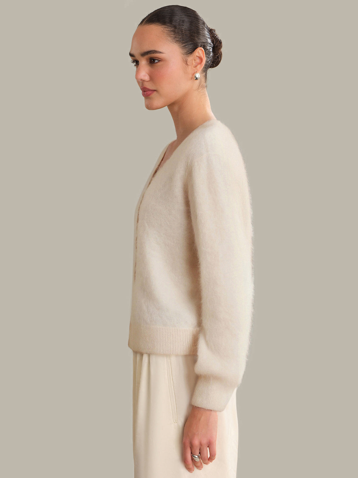 Woman wearing a beige cardigan and pants against a plain background