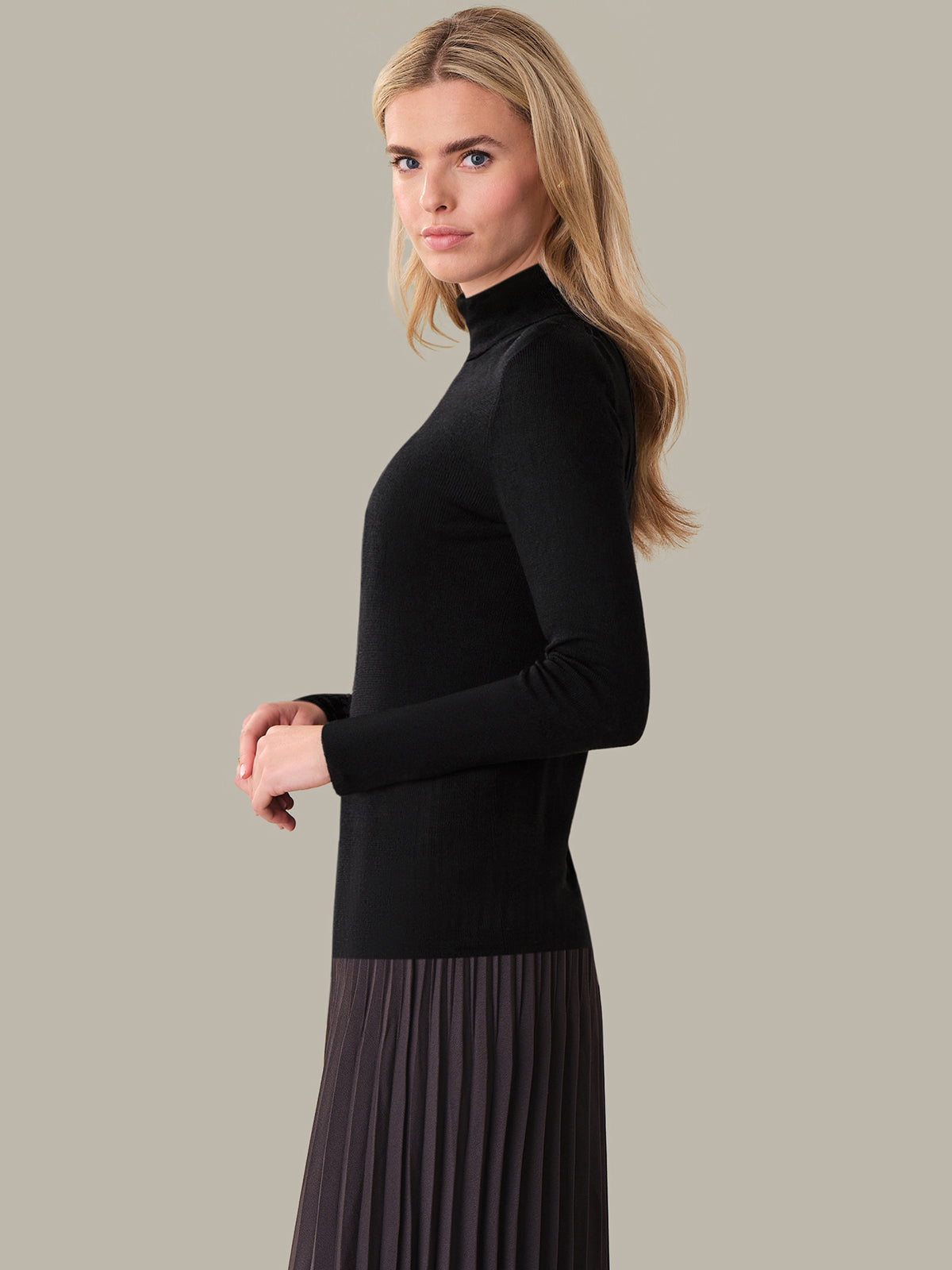 Woman wearing a black turtleneck and pleated skirt on a beige background